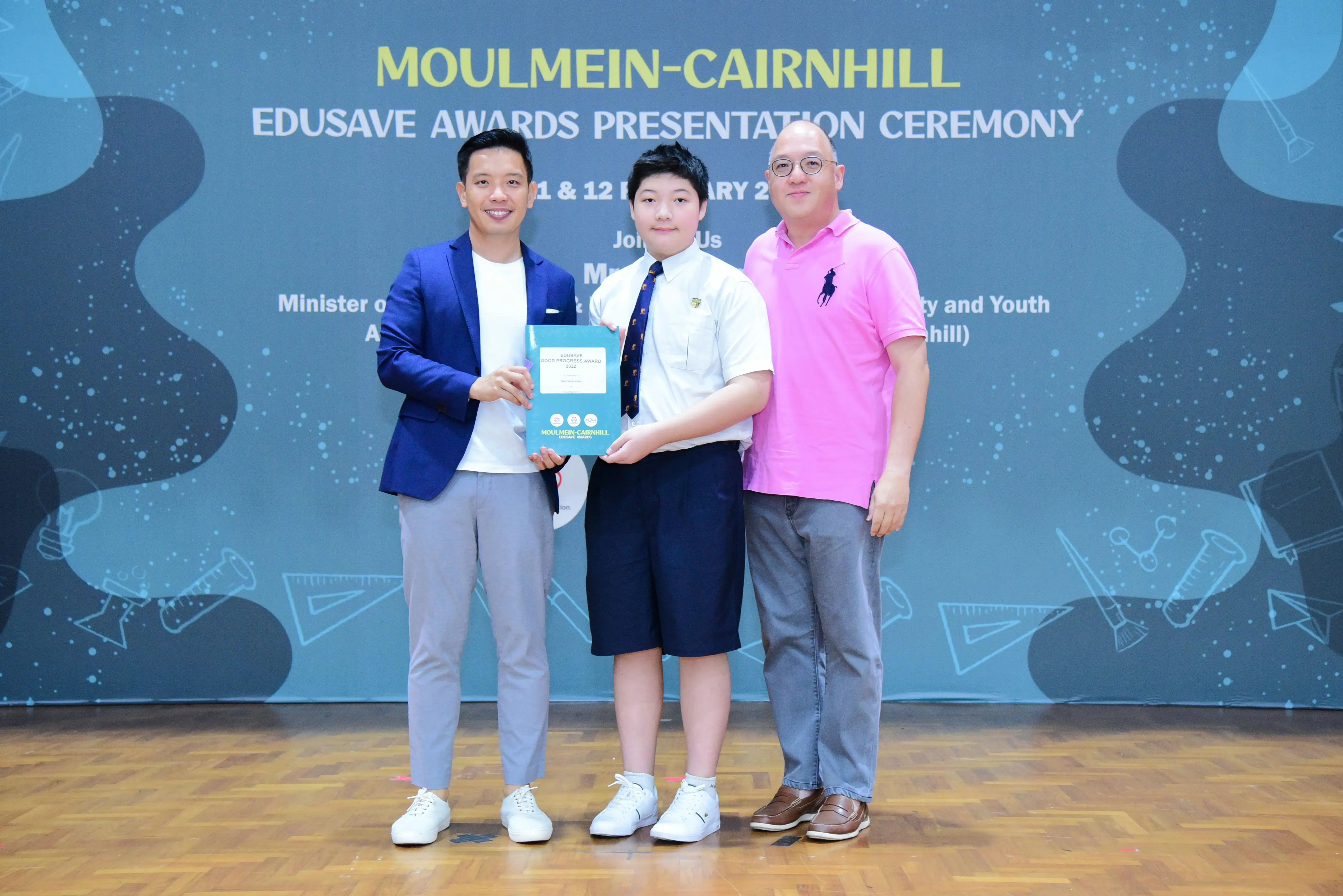 Three people pose at the Moulmein-Cairnhill Edusave Awards Presentation Ceremony, with a student holding an award certificate.