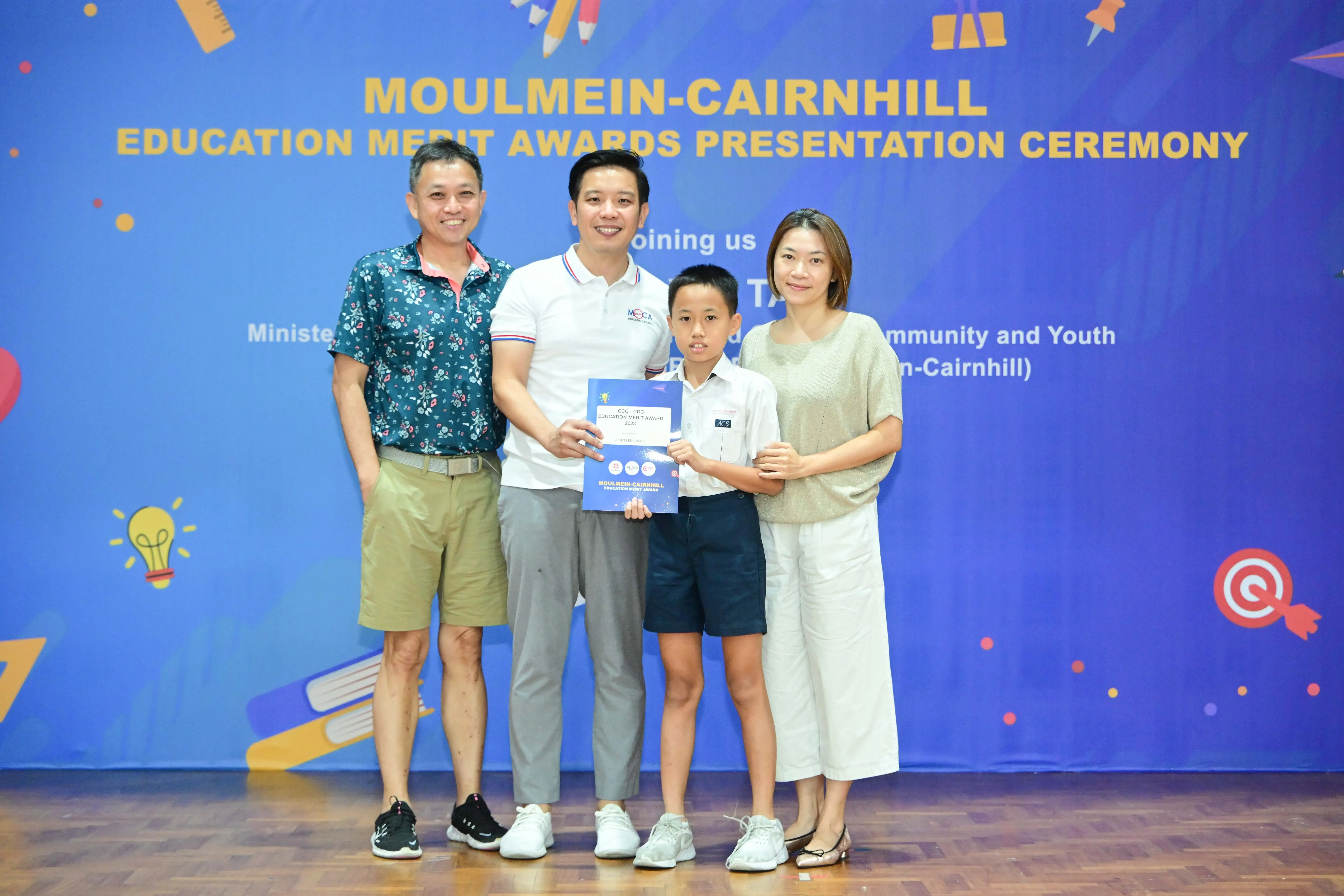 Three adults and a boy hold an award certificate at the Moulmein-Cairnhill Education Merit Awards Presentation Ceremony.