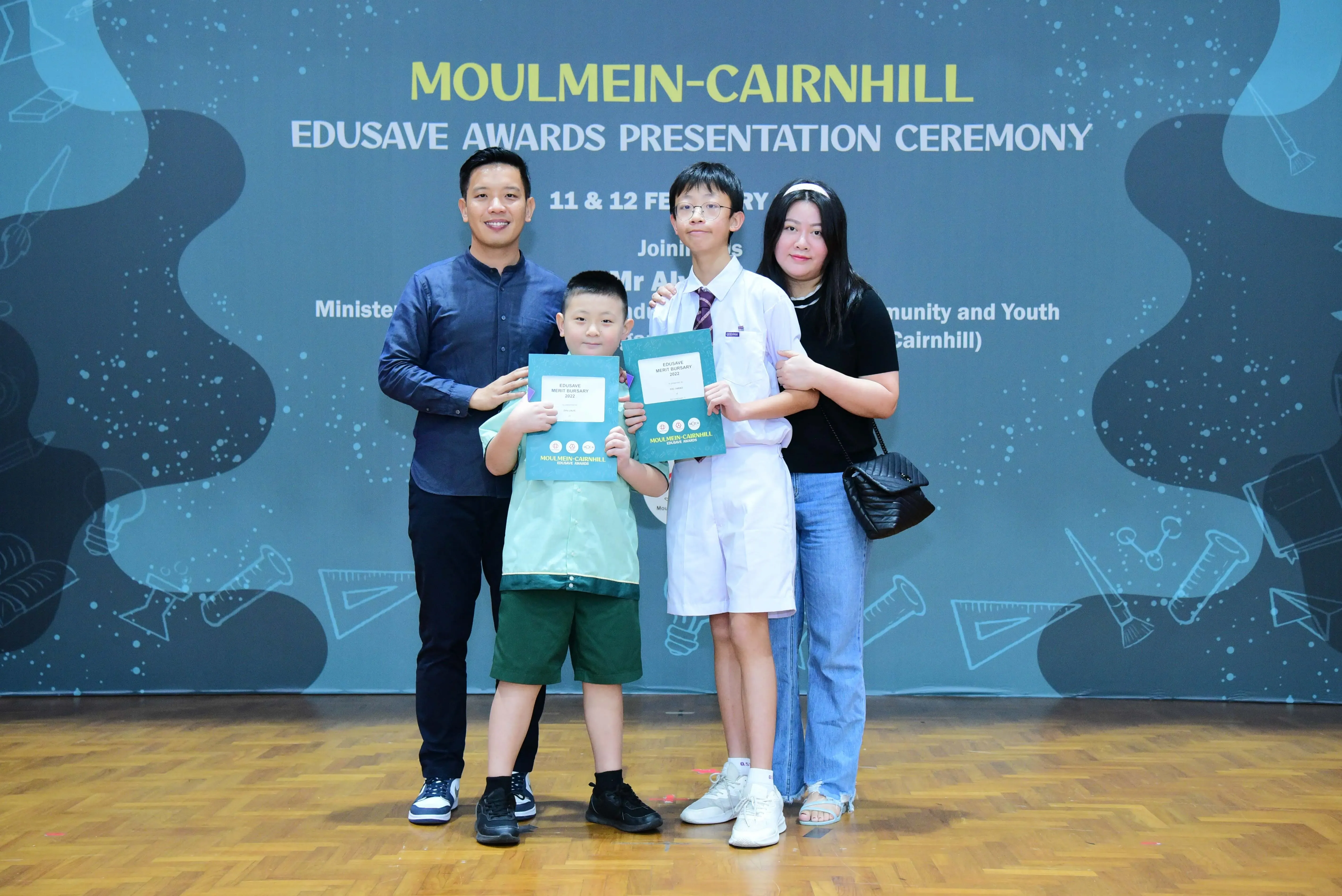 Two adults and two children pose with award folders at the Moulmein-Cairnhill Edusave Awards Presentation Ceremony.