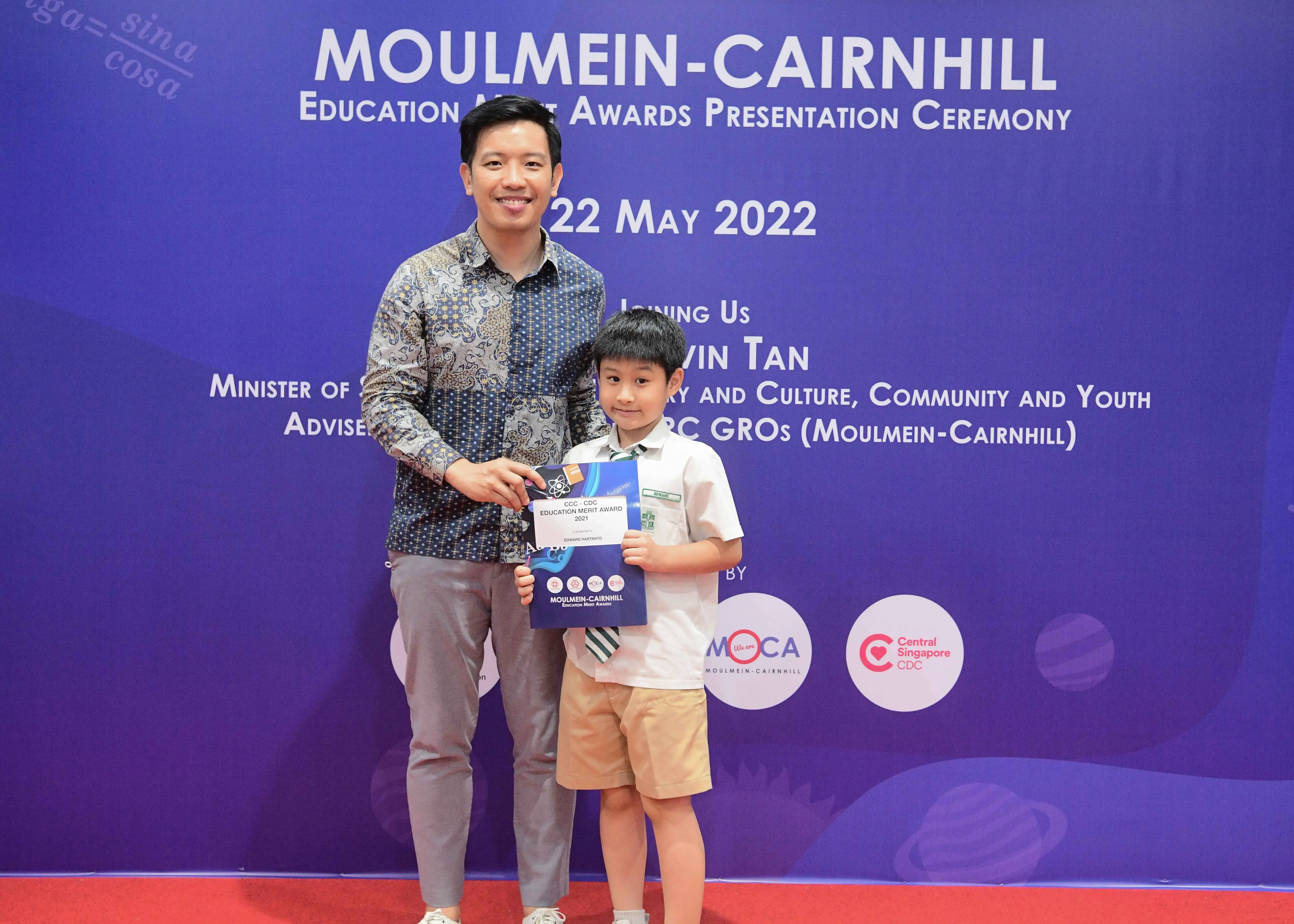 A man and a young boy pose holding an award certificate at the Moulmein-Cairnhill Education Merit Awards ceremony on 22 May 2022.