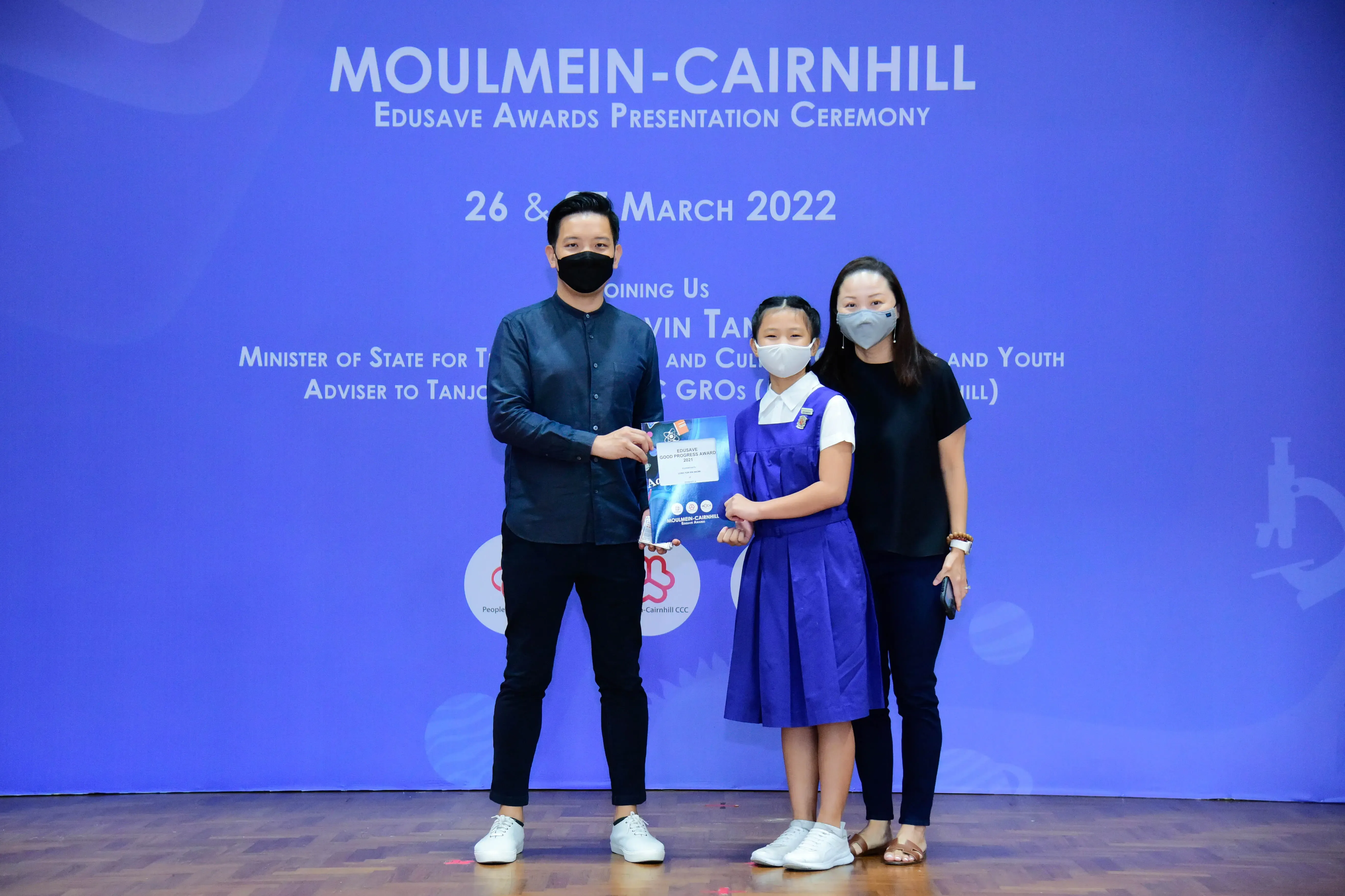 A man, a young girl in a blue school uniform, and a woman pose at the Moulmein-Cairnhill Edusave Awards ceremony in 2022.