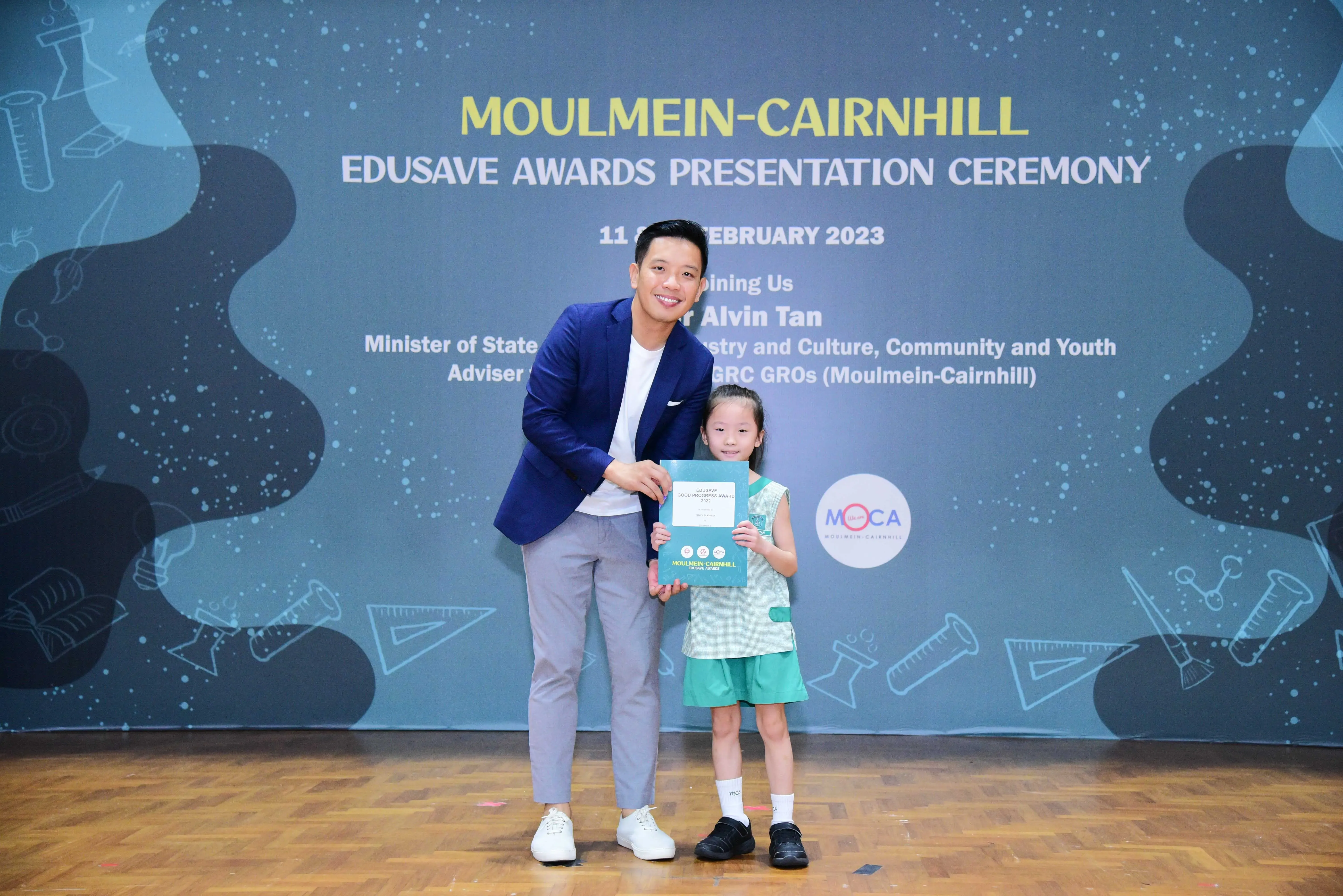 A man in a blue blazer and a young girl hold a certificate at the Moulmein-Cairnhill Edusave Awards Ceremony 2023.