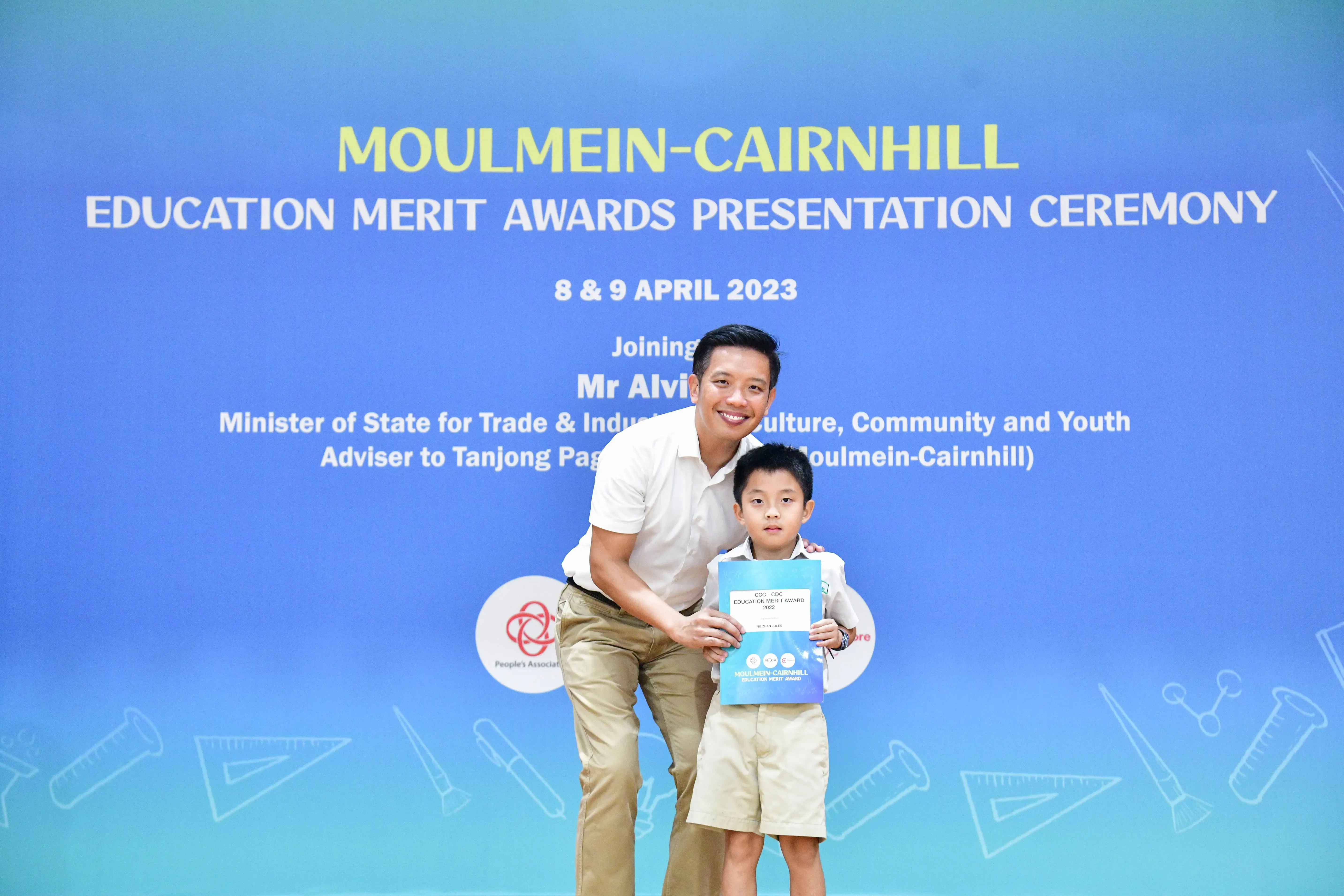 A man and young boy pose holding an award certificate at the Moulmein-Cairnhill Education Merit Awards Ceremony, April 2023.