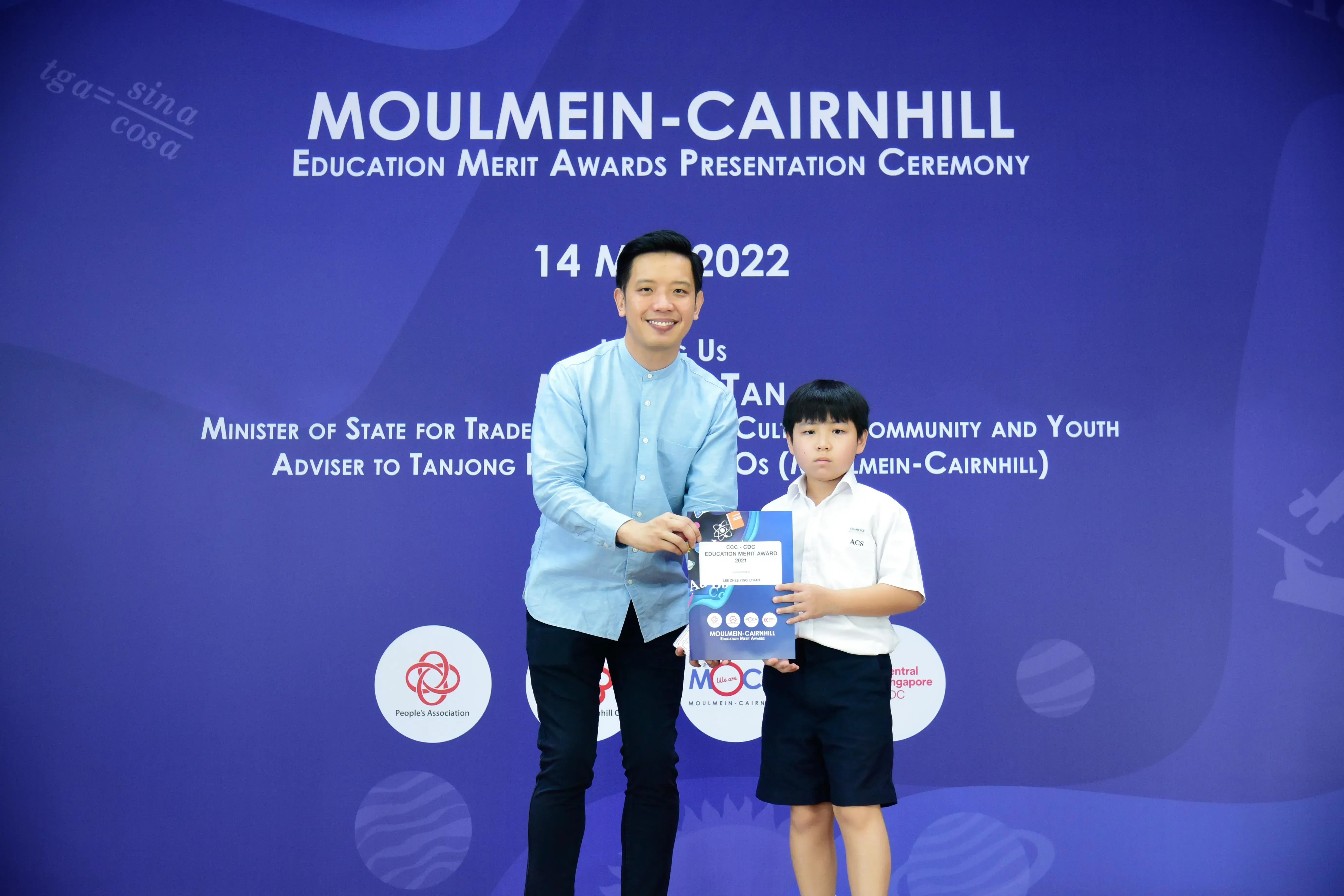 An adult man and a young boy hold an award certificate at the Moulmein-Cairnhill Education Merit Awards 2022.