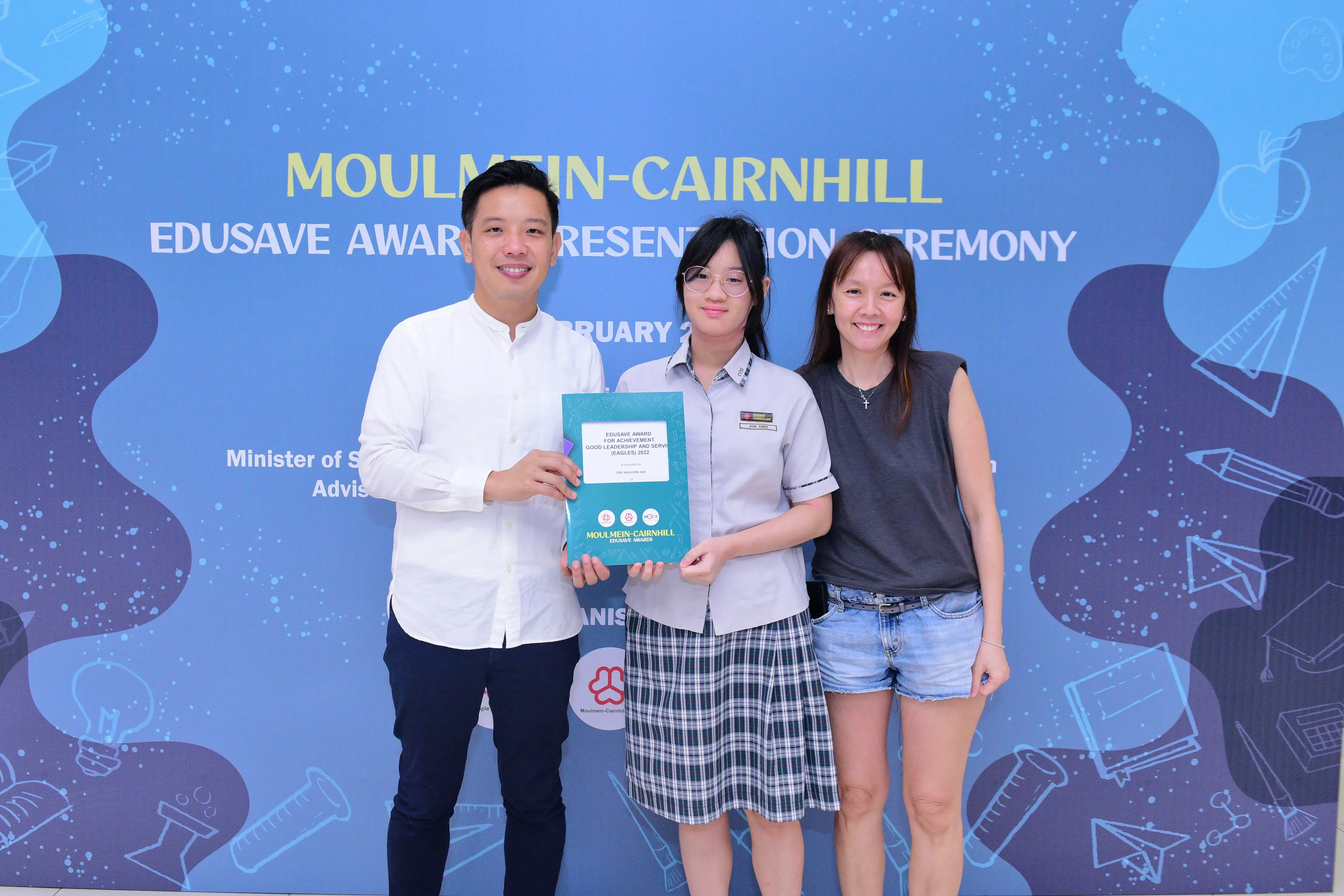 Three people pose at the Moulmein-Cairnhill Edusave Award Presentation Ceremony, with a student holding a certificate.