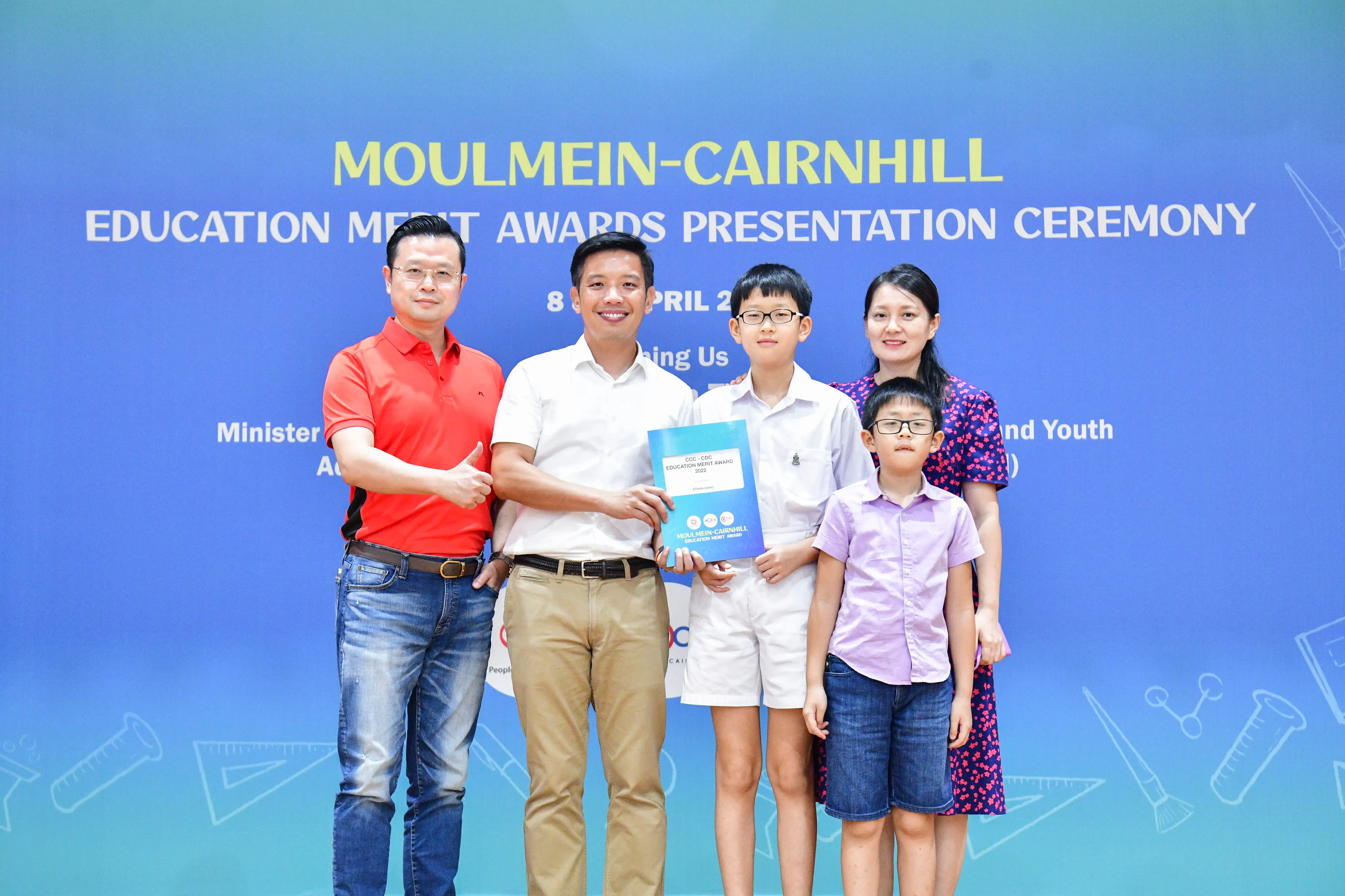 Five people pose at the Moulmein-Cairnhill Education Merit Awards Presentation Ceremony, with a boy holding an award certificate.