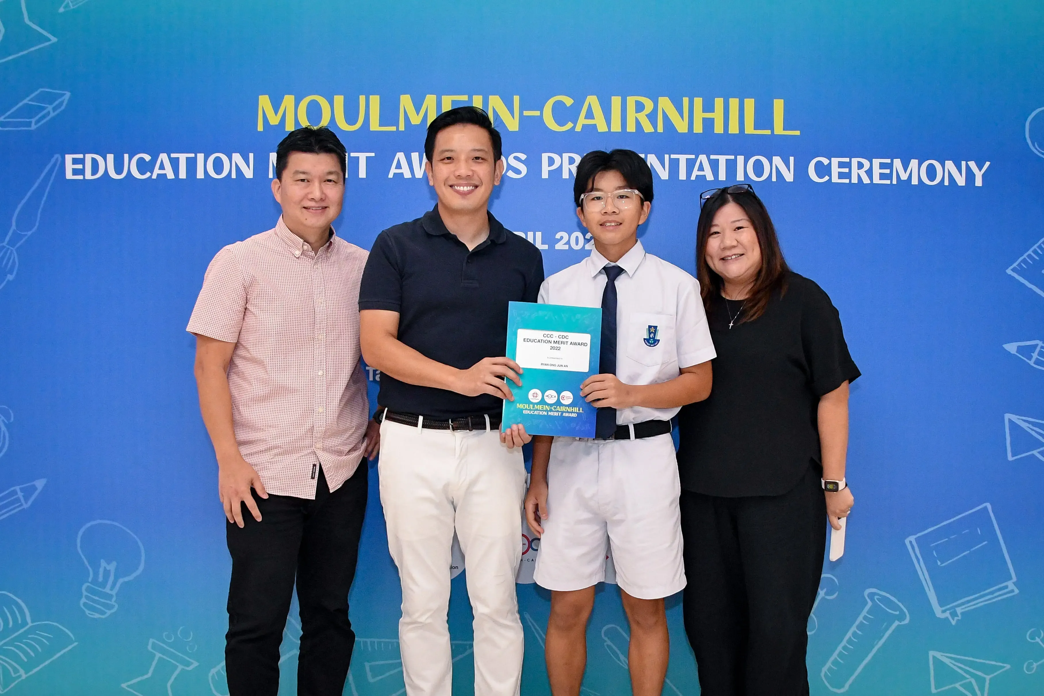Four people pose at the Moulmein-Cairnhill Education Merit Awards Presentation Ceremony, holding an award booklet.