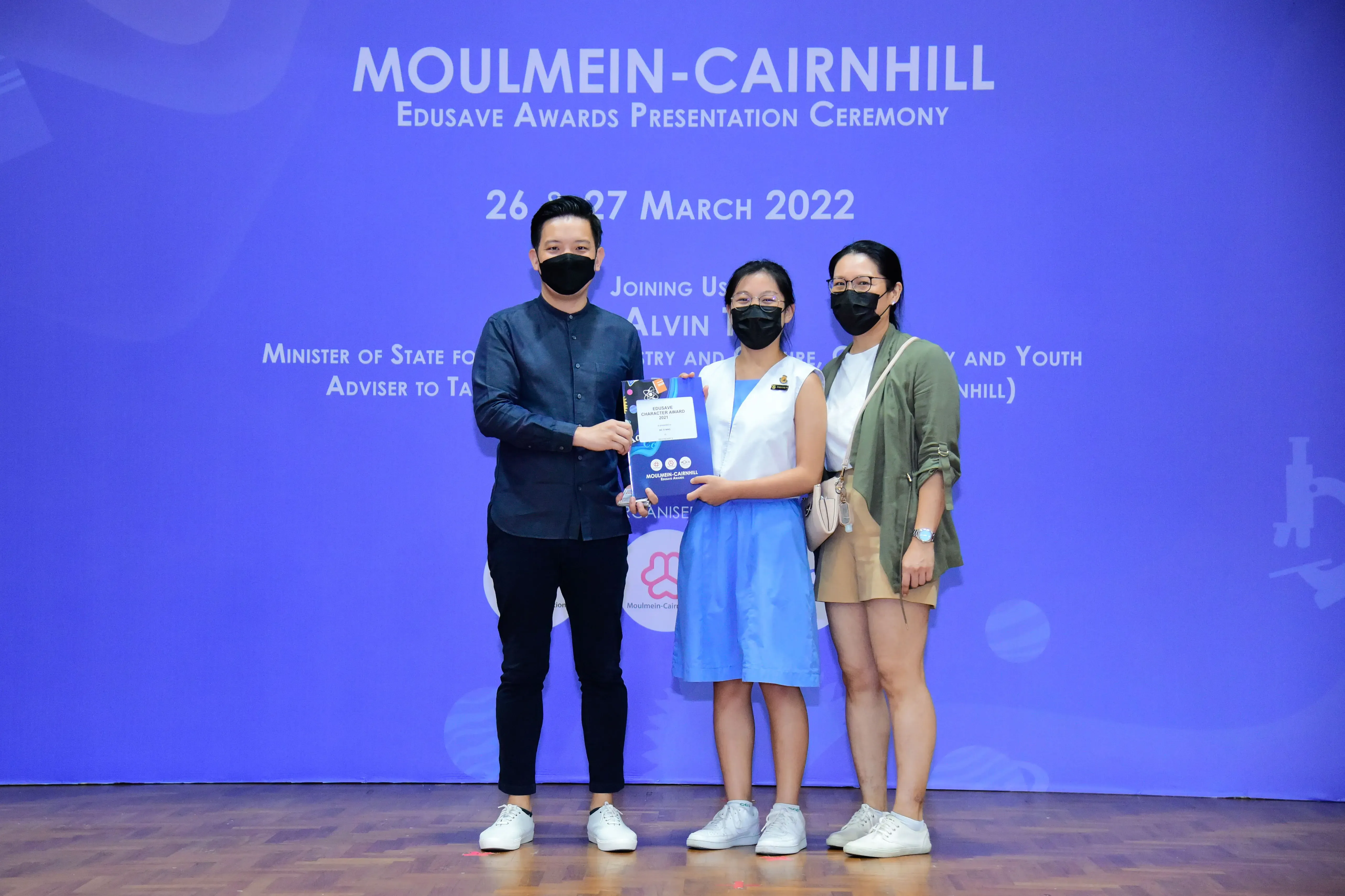 Three masked people pose holding an award at the Moulmein-Cairnhill Edusave Awards Ceremony, March 2022.
