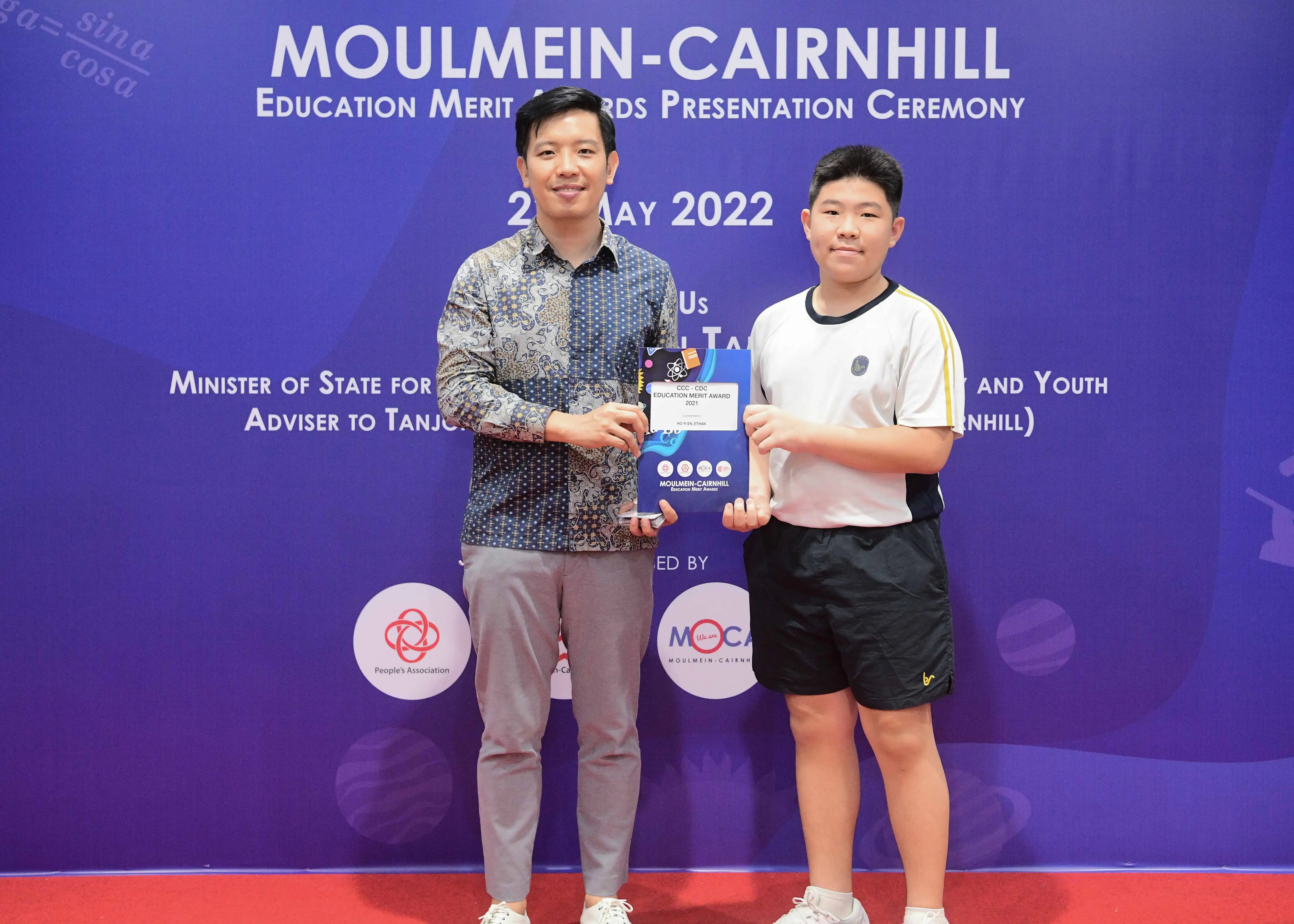 Two people pose holding an award at the Moulmein-Cairnhill Education Merit Awards Ceremony, May 2022.