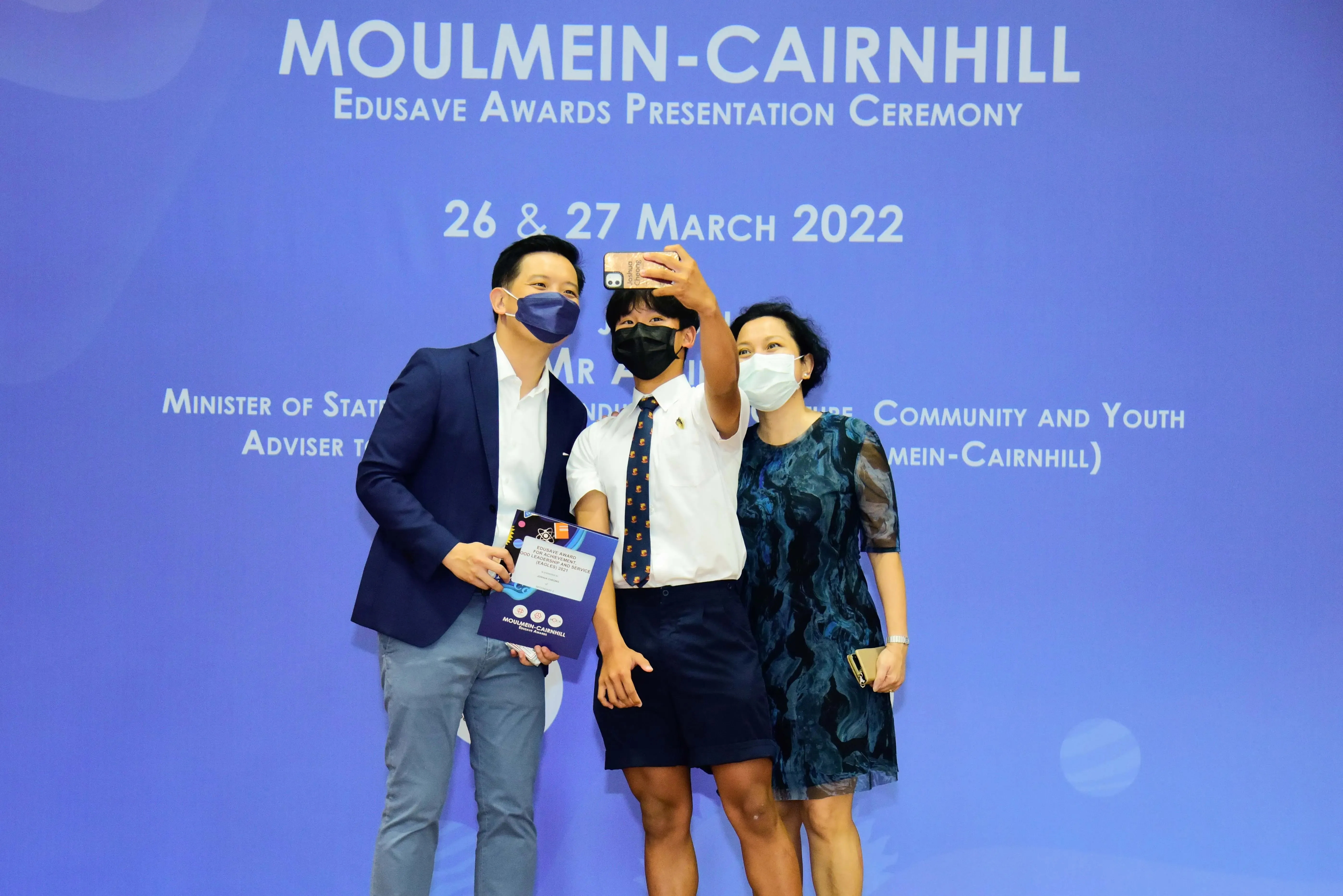 Three masked people take a selfie at the Moulmein-Cairnhill Edusave Awards Presentation Ceremony in March 2022.