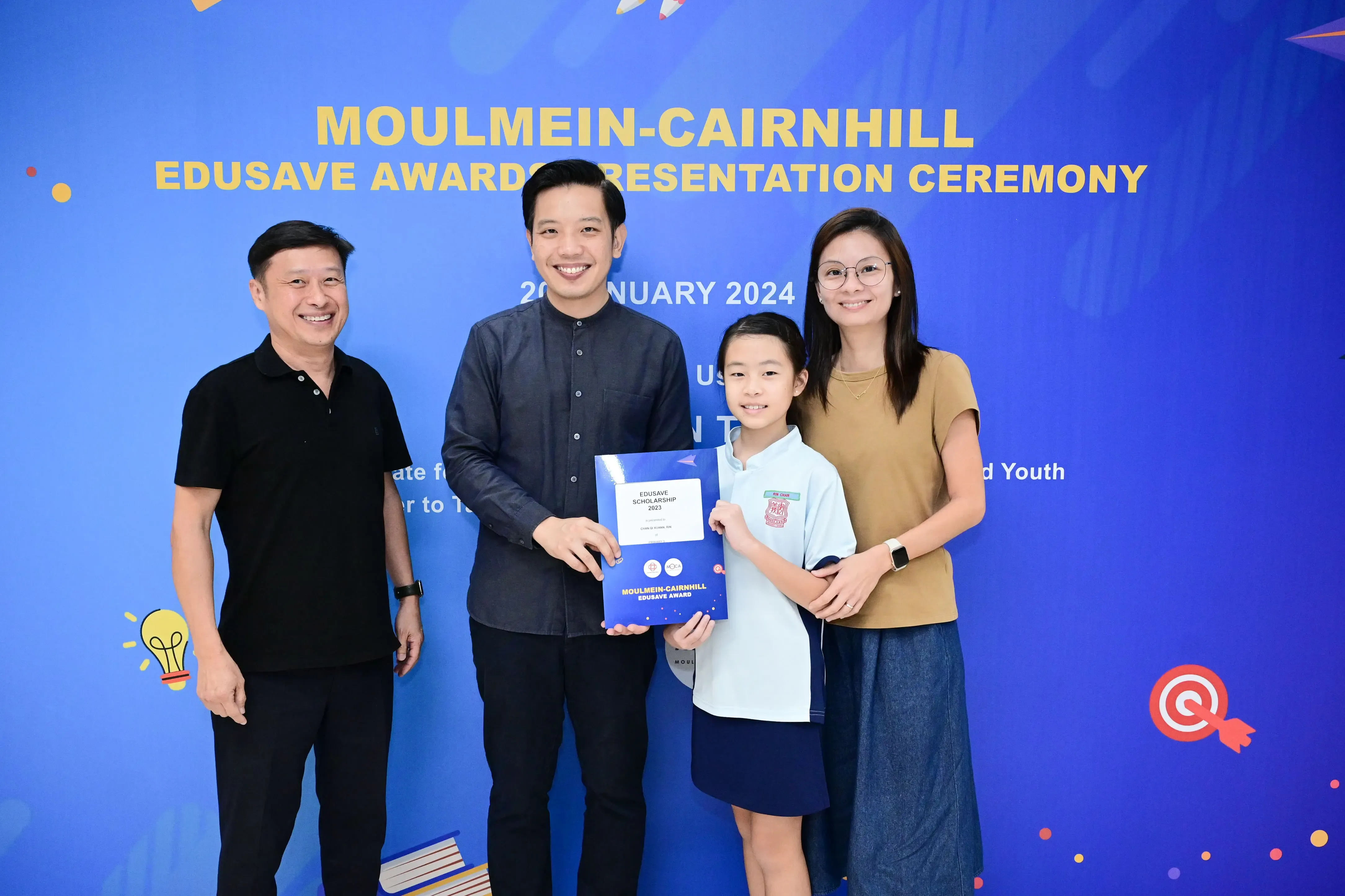Three adults and a child pose with an Edusave Scholarship certificate at the Moulmein-Cairnhill Awards Ceremony, January 2024.