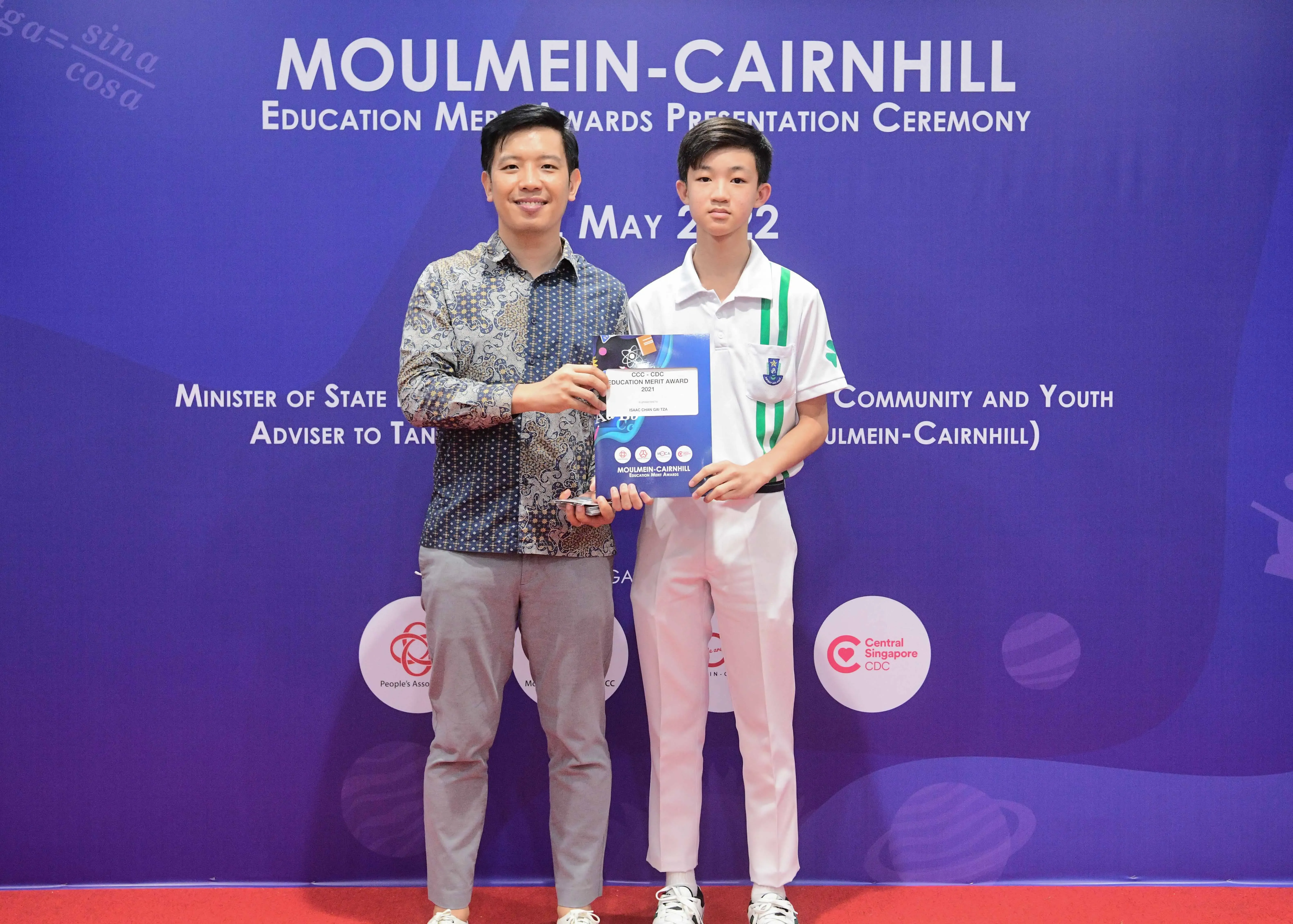 Two people pose holding an award certificate at the Moulmein-Cairnhill Education Merit Awards Presentation Ceremony, May 2022.