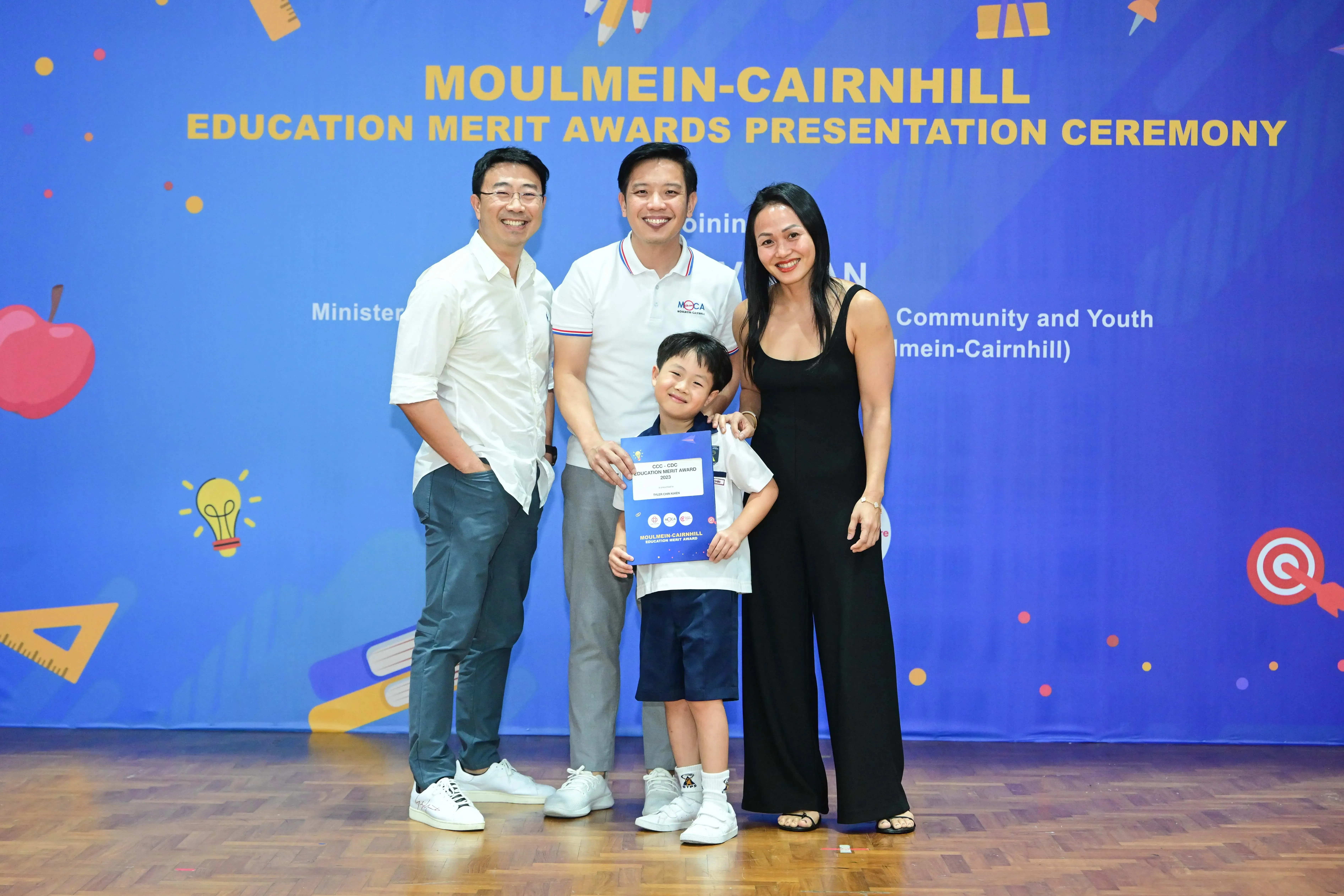 Three adults and a young boy pose with an award certificate at the Moulmein-Cairnhill Education Merit Awards ceremony.