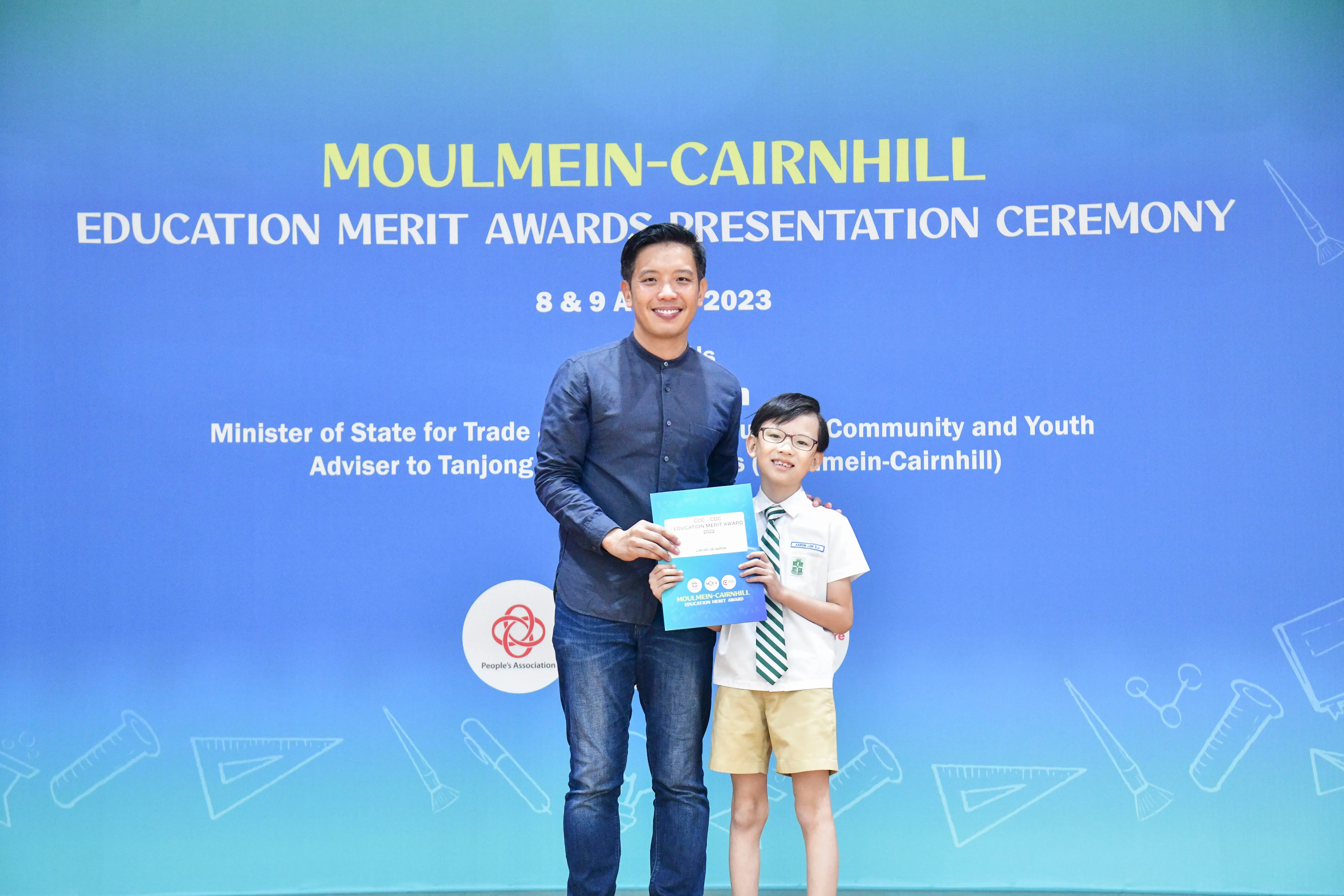 A man and a young boy hold a certificate at the Moulmein-Cairnhill Education Merit Awards Ceremony 2023.