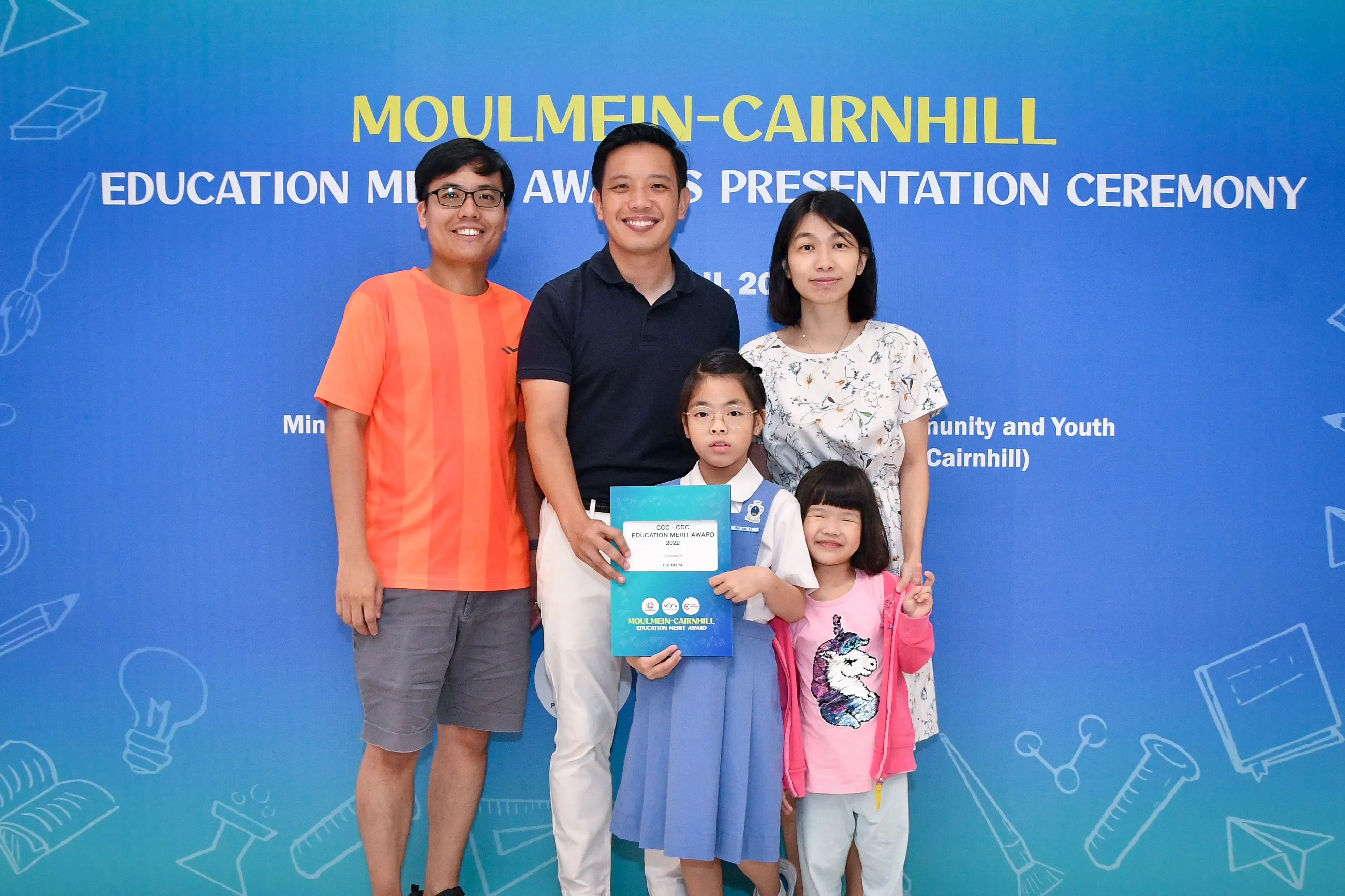 Five people pose at the Moulmein-Cairnhill Education Merit Awards Presentation Ceremony, with a girl holding an award certificate.