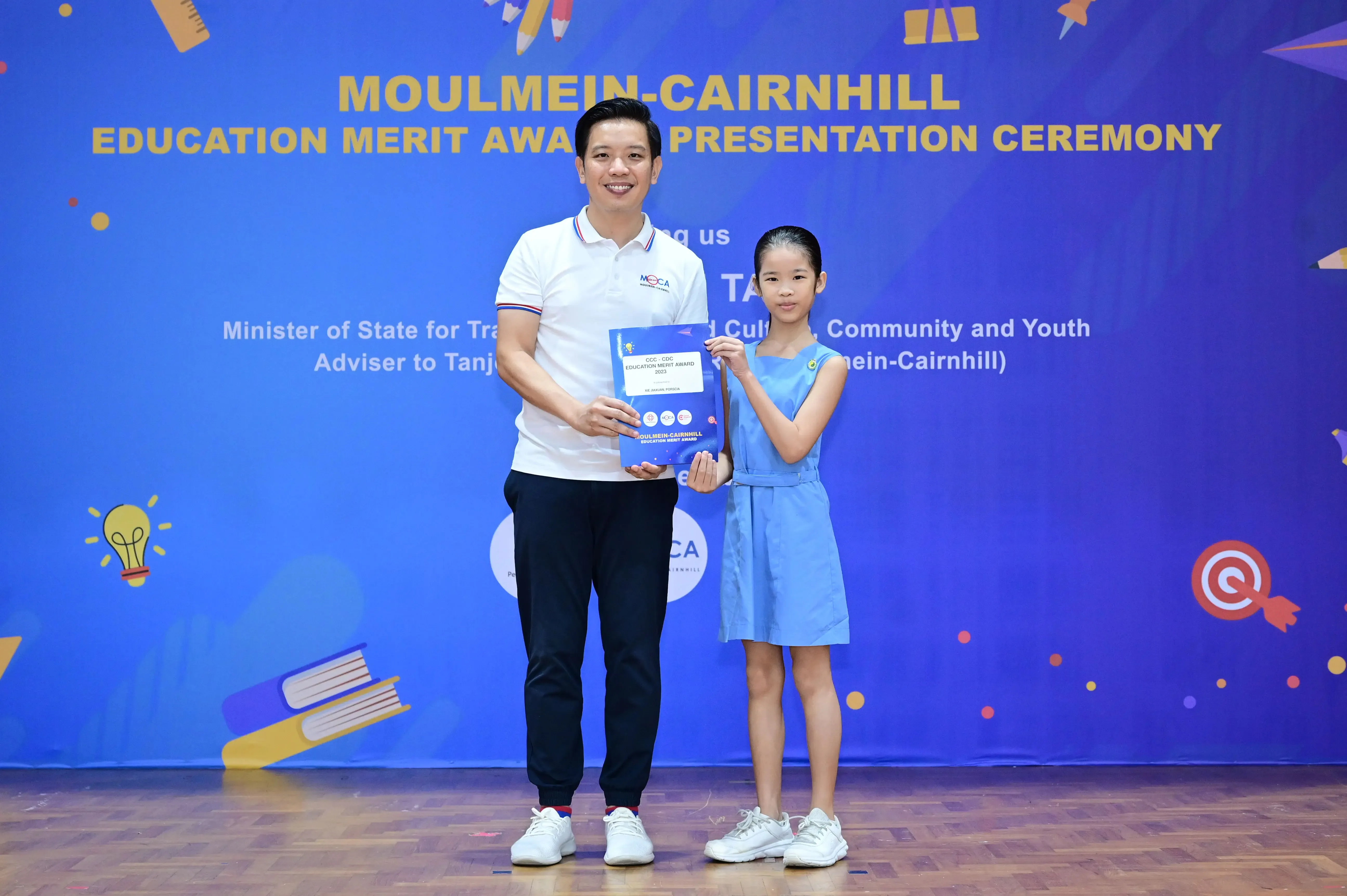 A man and a girl hold an award certificate at the Moulmein-Cairnhill Education Merit Award Presentation Ceremony.