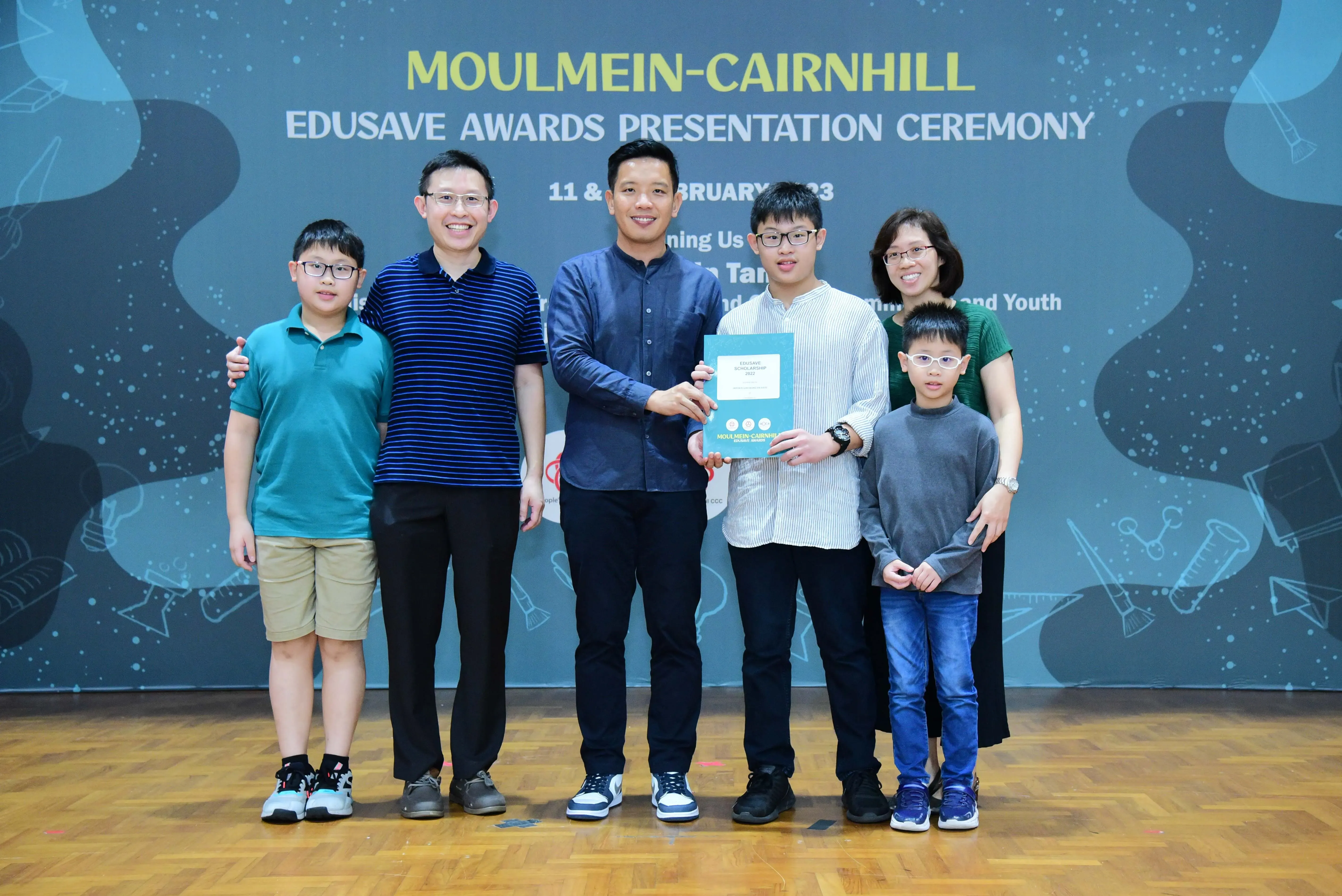 Six people pose at the Moulmein-Cairnhill Edusave Awards Presentation Ceremony, with a teen holding a certificate.