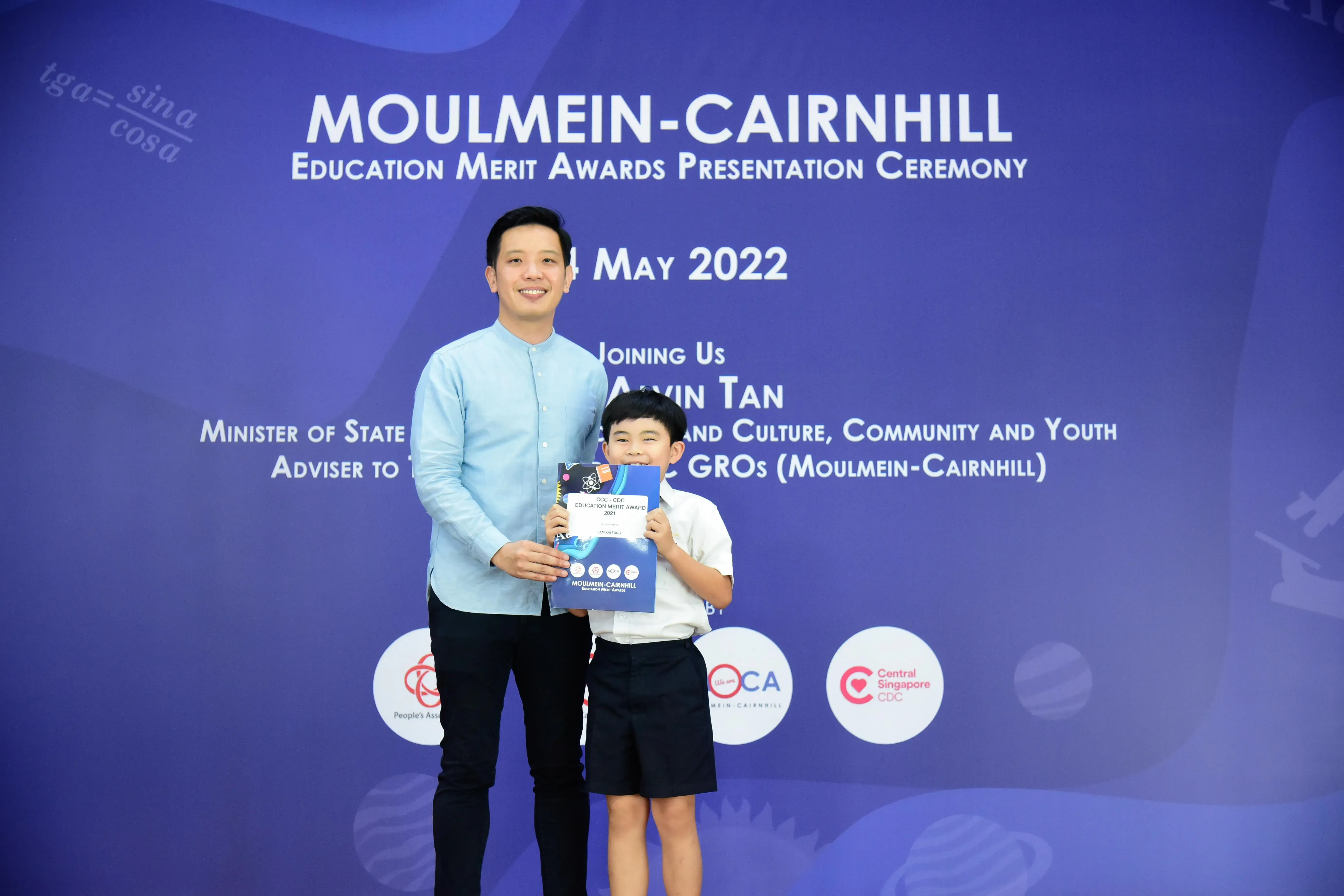A man and a young boy pose holding an award certificate at the Moulmein-Cairnhill Education Merit Awards ceremony, May 2022.