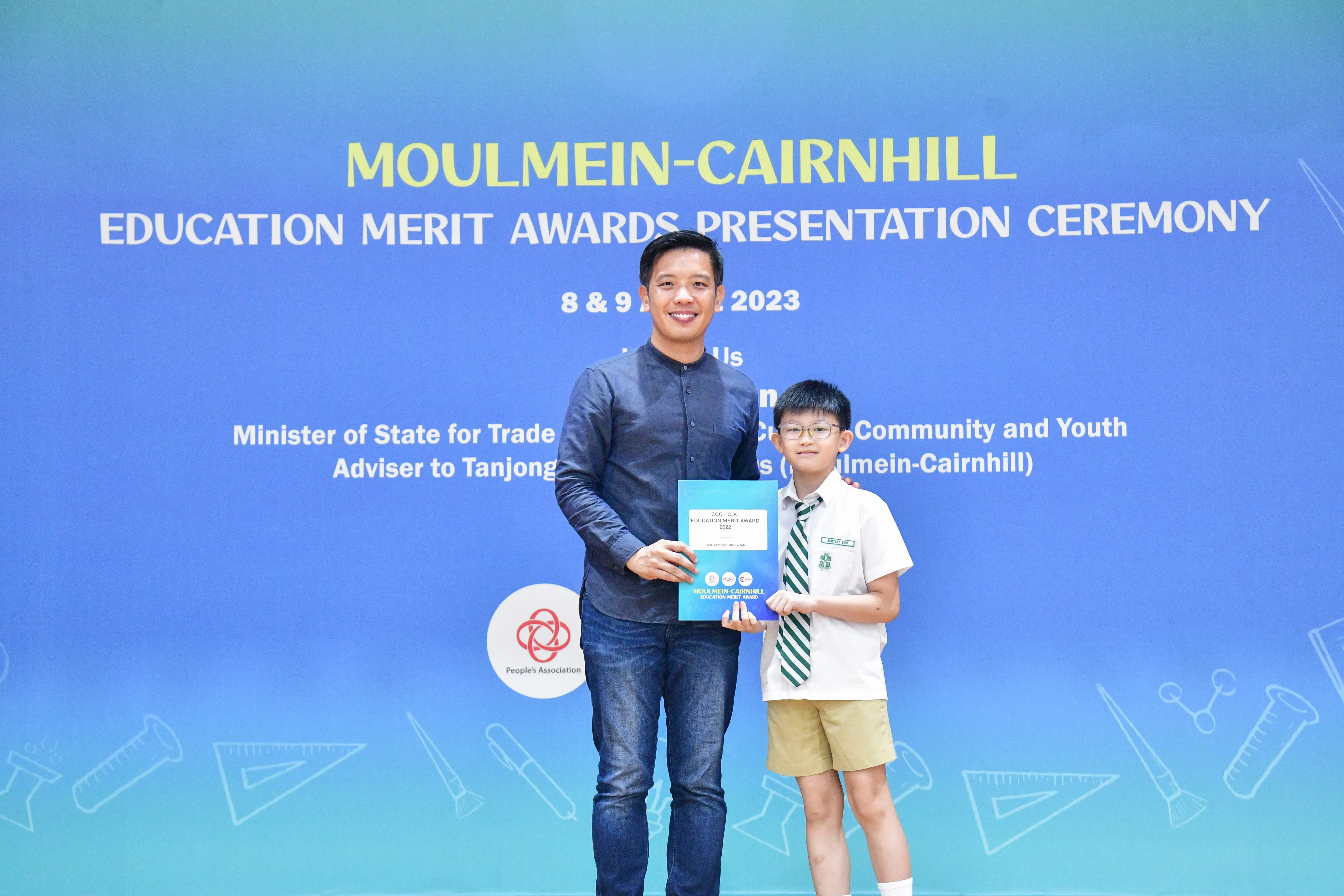 An adult and a young boy in school uniform hold a certificate at the Moulmein-Cairnhill Education Merit Awards 2023.
