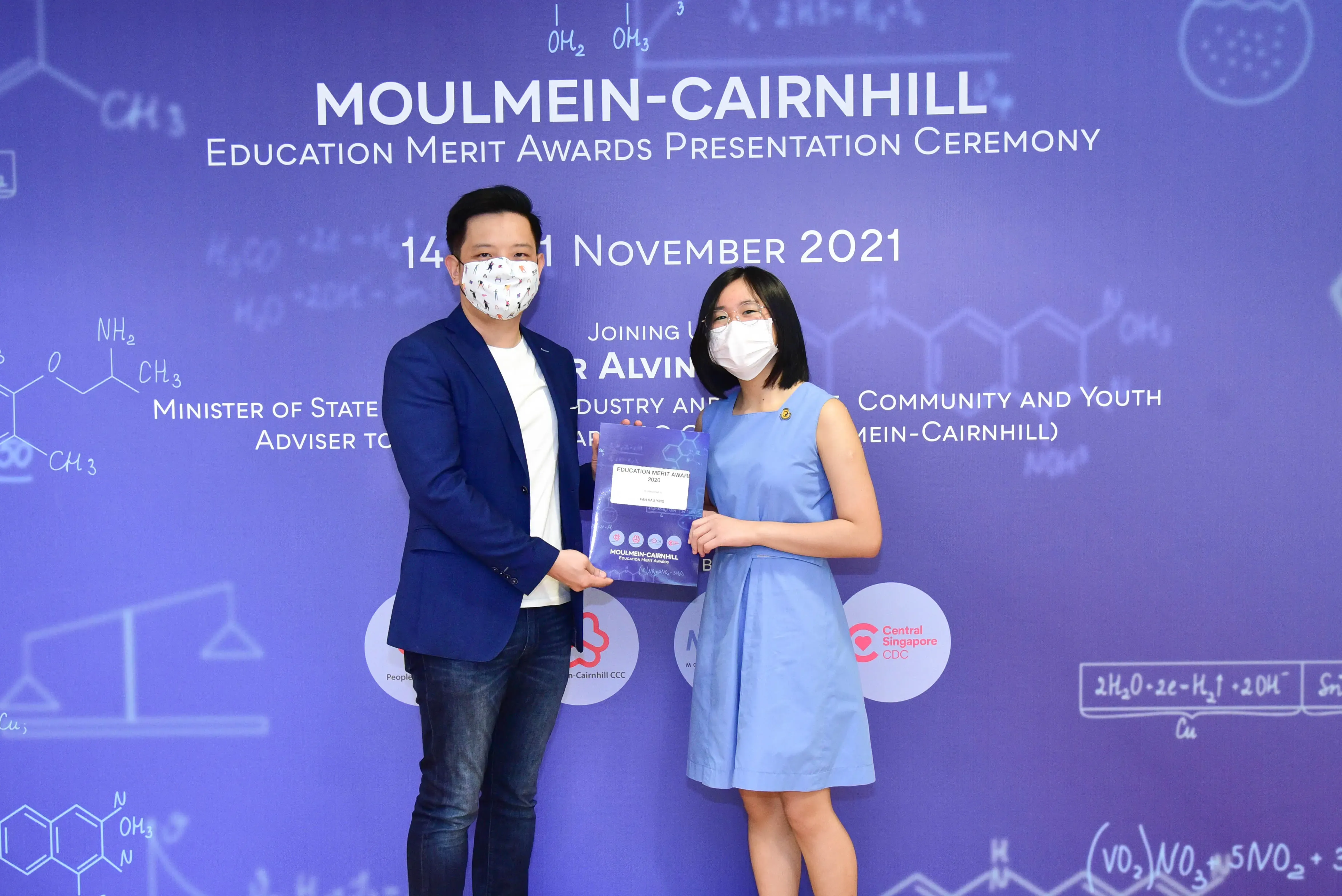 Two masked people hold an award folder at the Moulmein-Cairnhill Education Merit Awards Ceremony, November 2021.