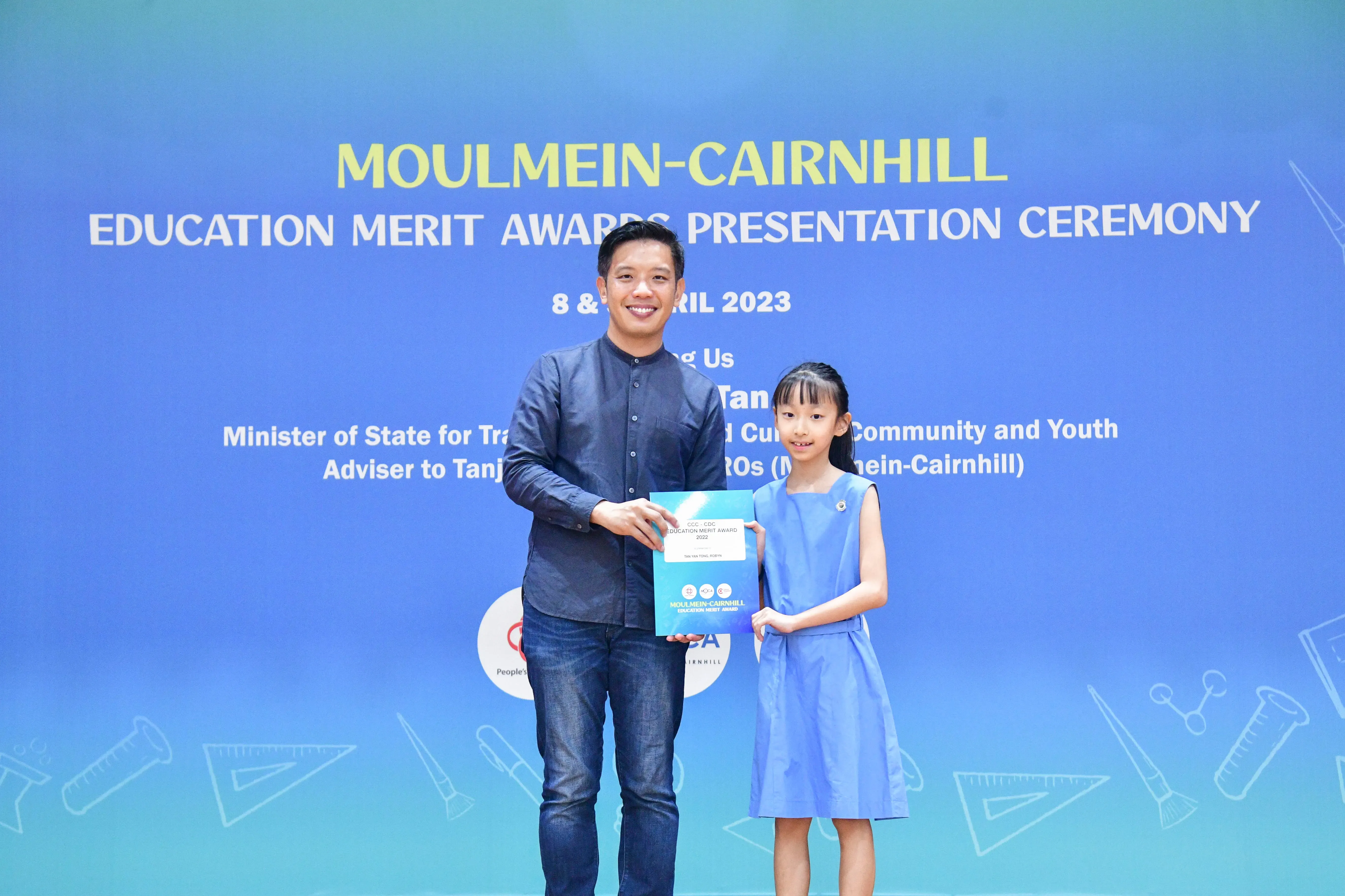A man and a young girl hold an award certificate at the Moulmein-Cairnhill Education Merit Awards Ceremony 2023.