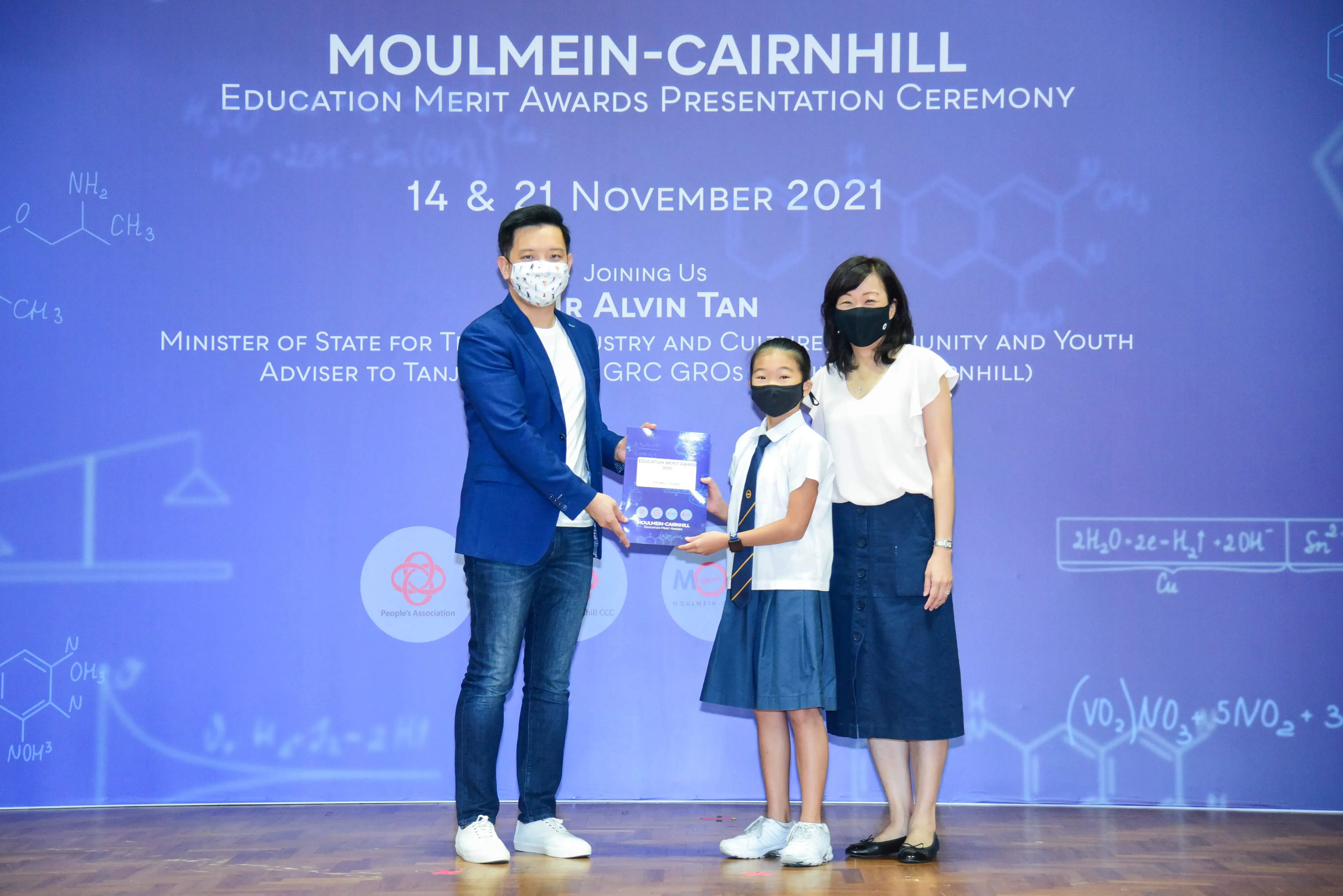 A man and woman present an award to a young student on stage at the Moulmein-Cairnhill Education Merit Awards 2021.