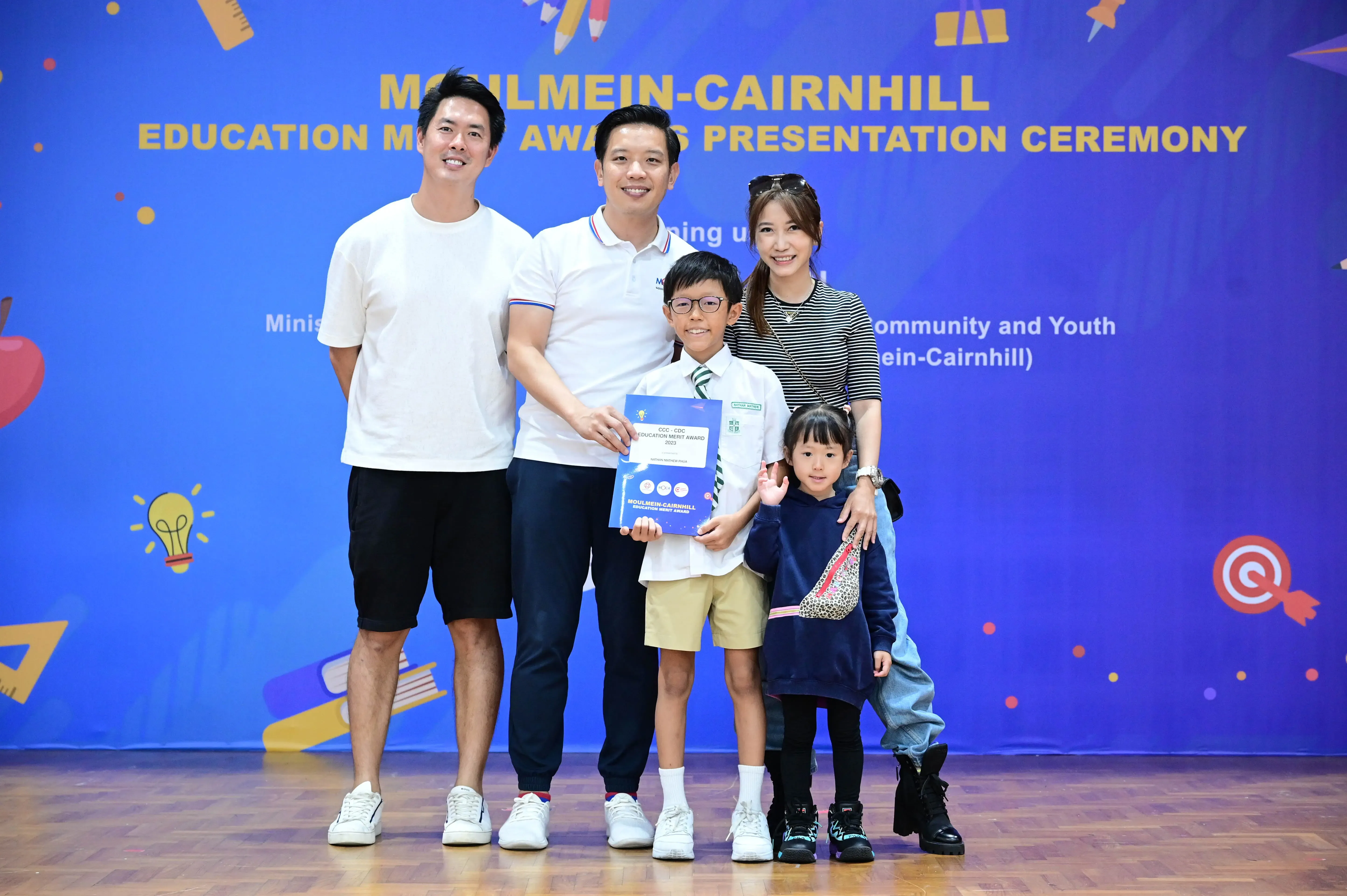 Three adults and two children pose with a merit award certificate at the Moulmein-Cairnhill Education Merit Awards ceremony.
