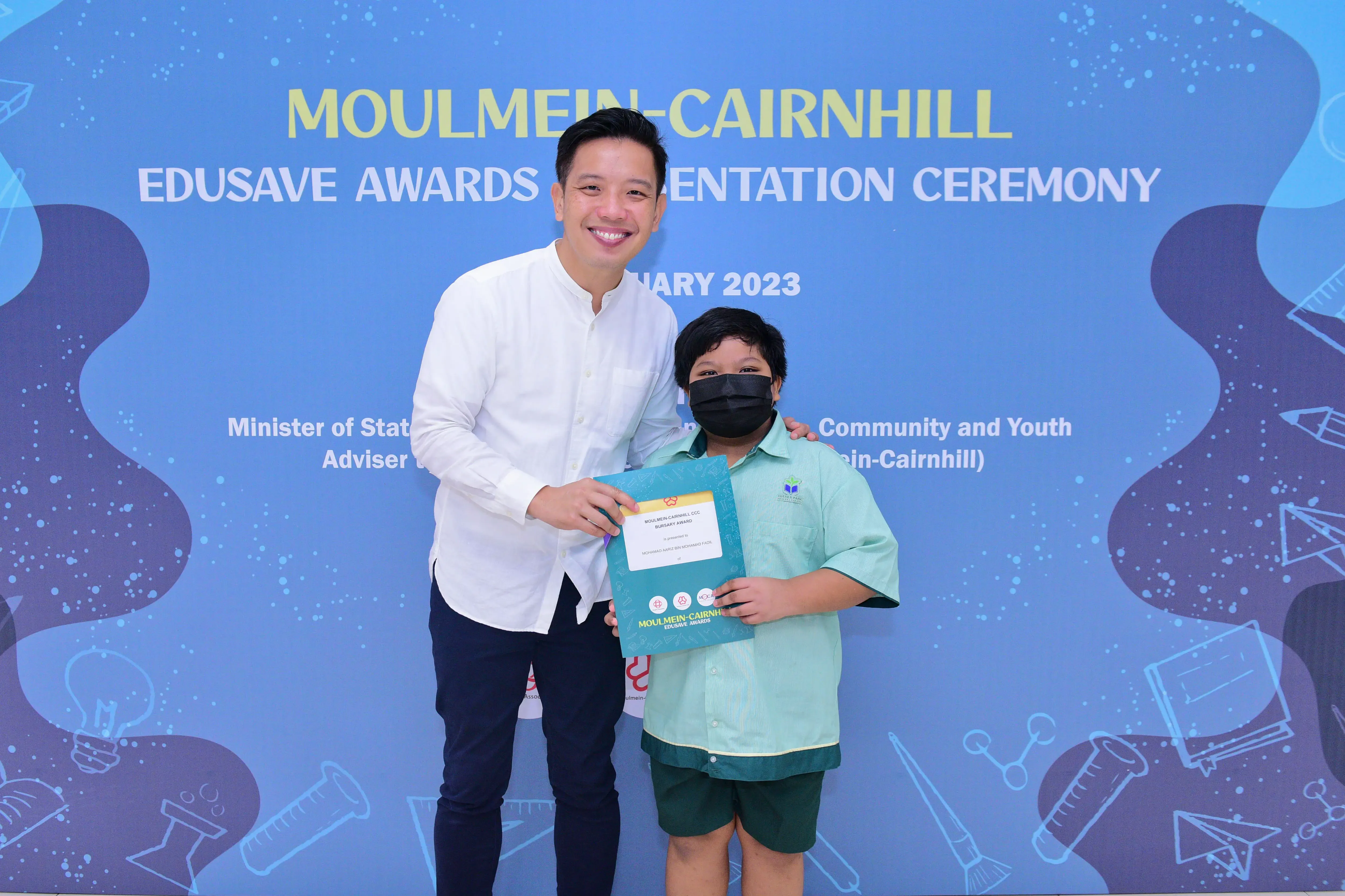 A man and a masked child hold a certificate at the Moulmein-Cairnhill Edusave Awards Presentation Ceremony 2023.
