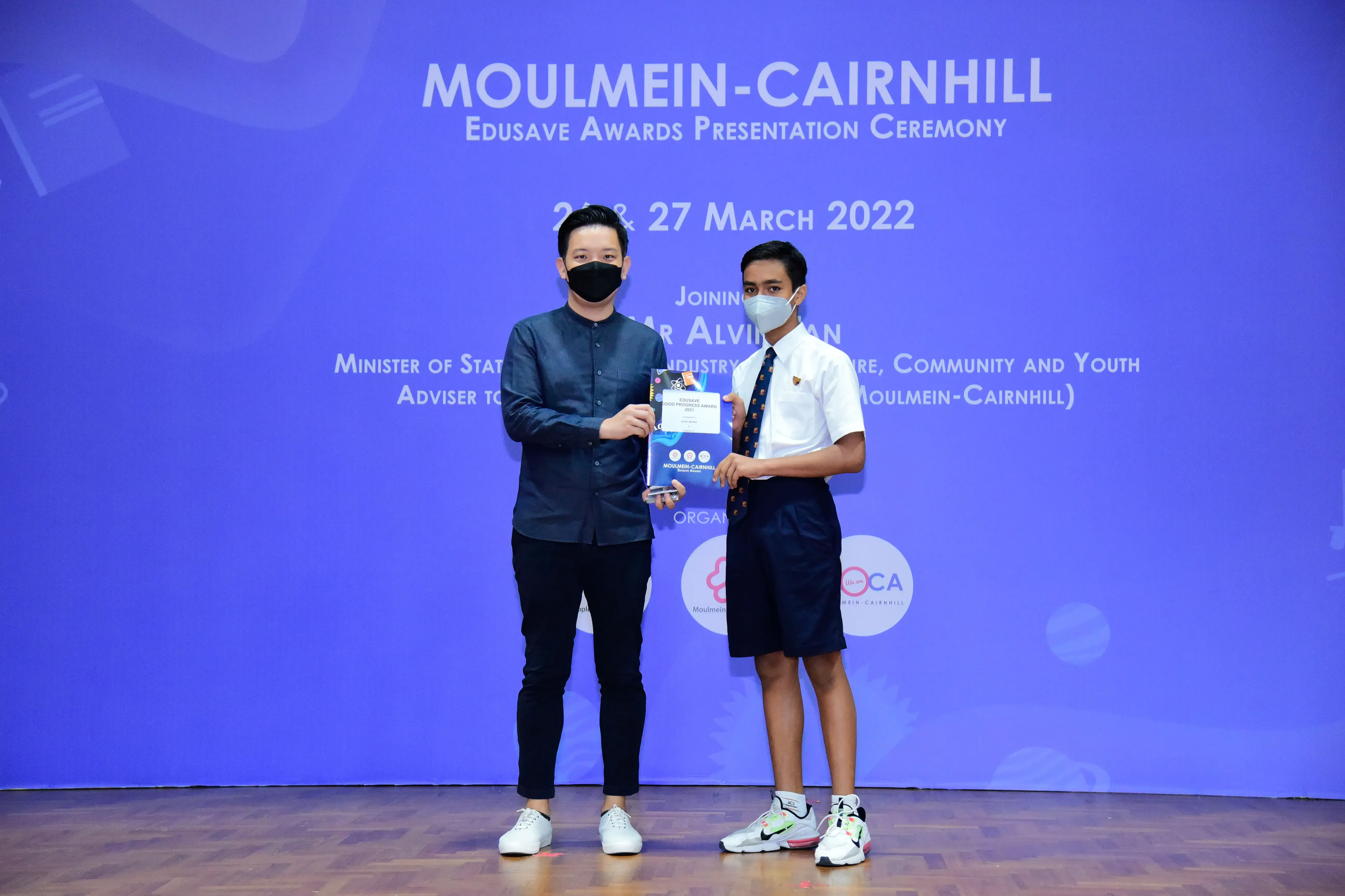 Two masked individuals hold an award at the Moulmein-Cairnhill Edusave Awards Presentation Ceremony, March 2022.