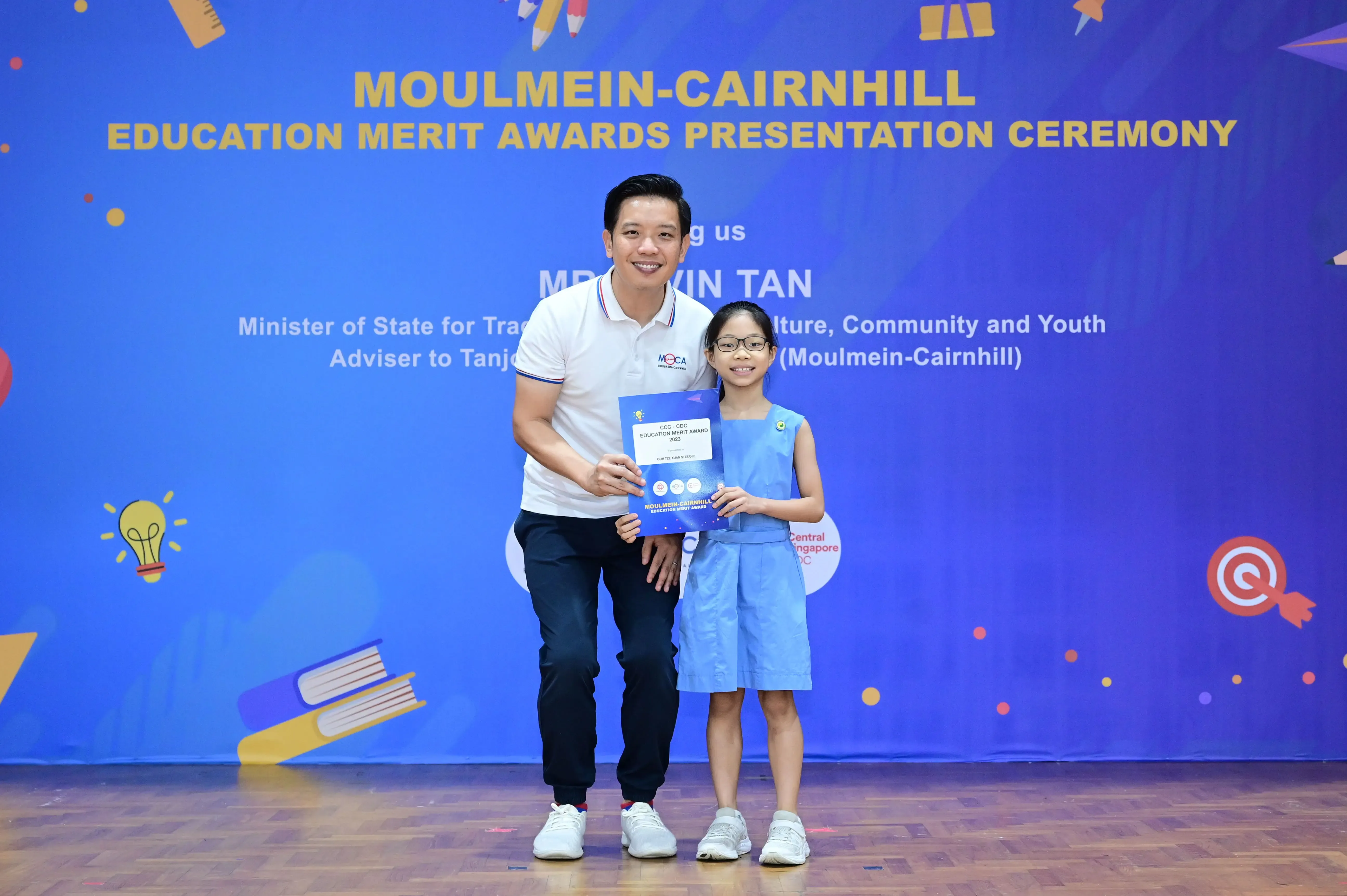 A man and a young girl holding an award certificate at the Moulmein-Cairnhill Education Merit Awards Presentation Ceremony.