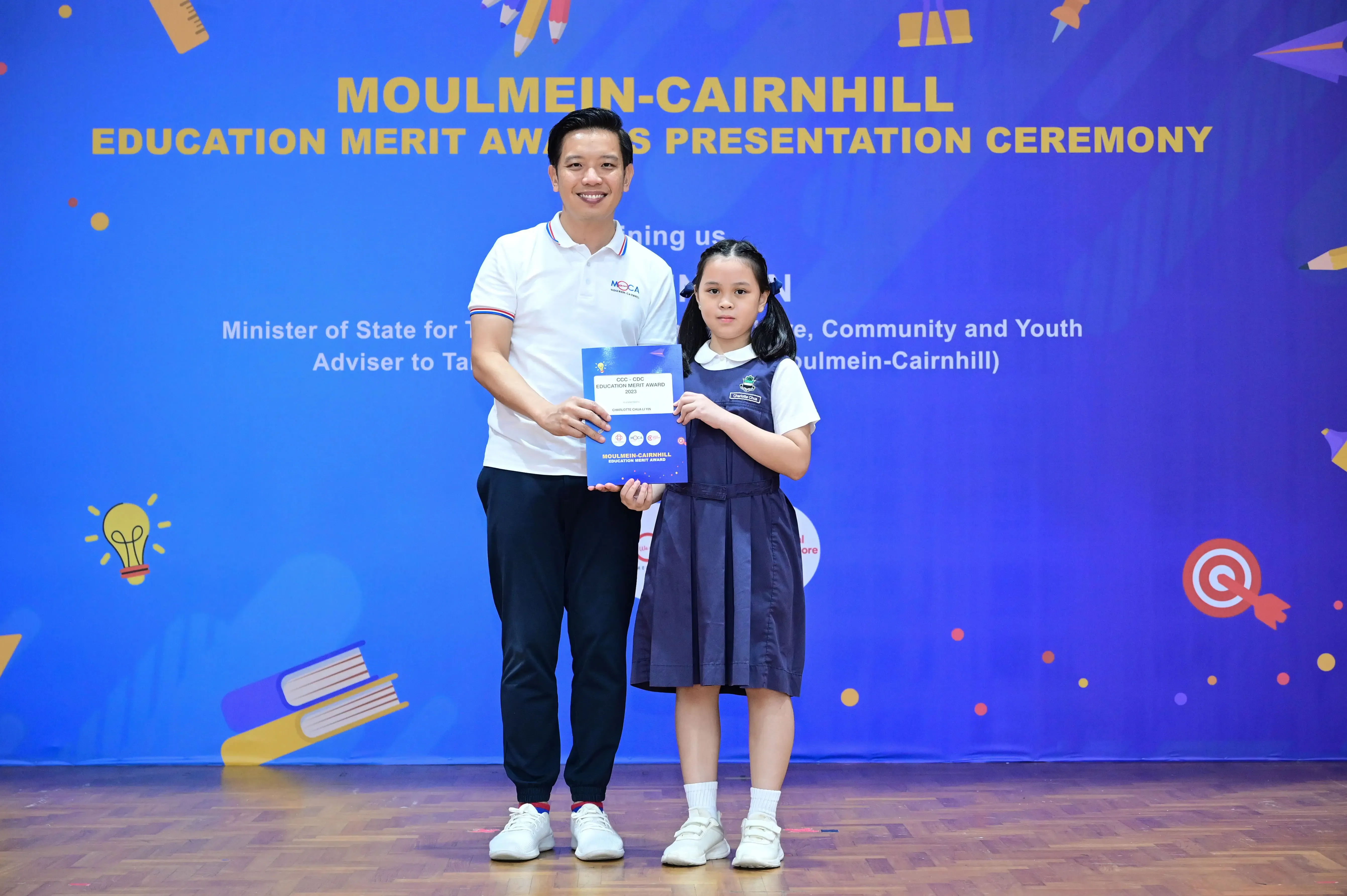A man and a young girl in school uniform hold a certificate at the Moulmein-Cairnhill Education Merit Awards ceremony.