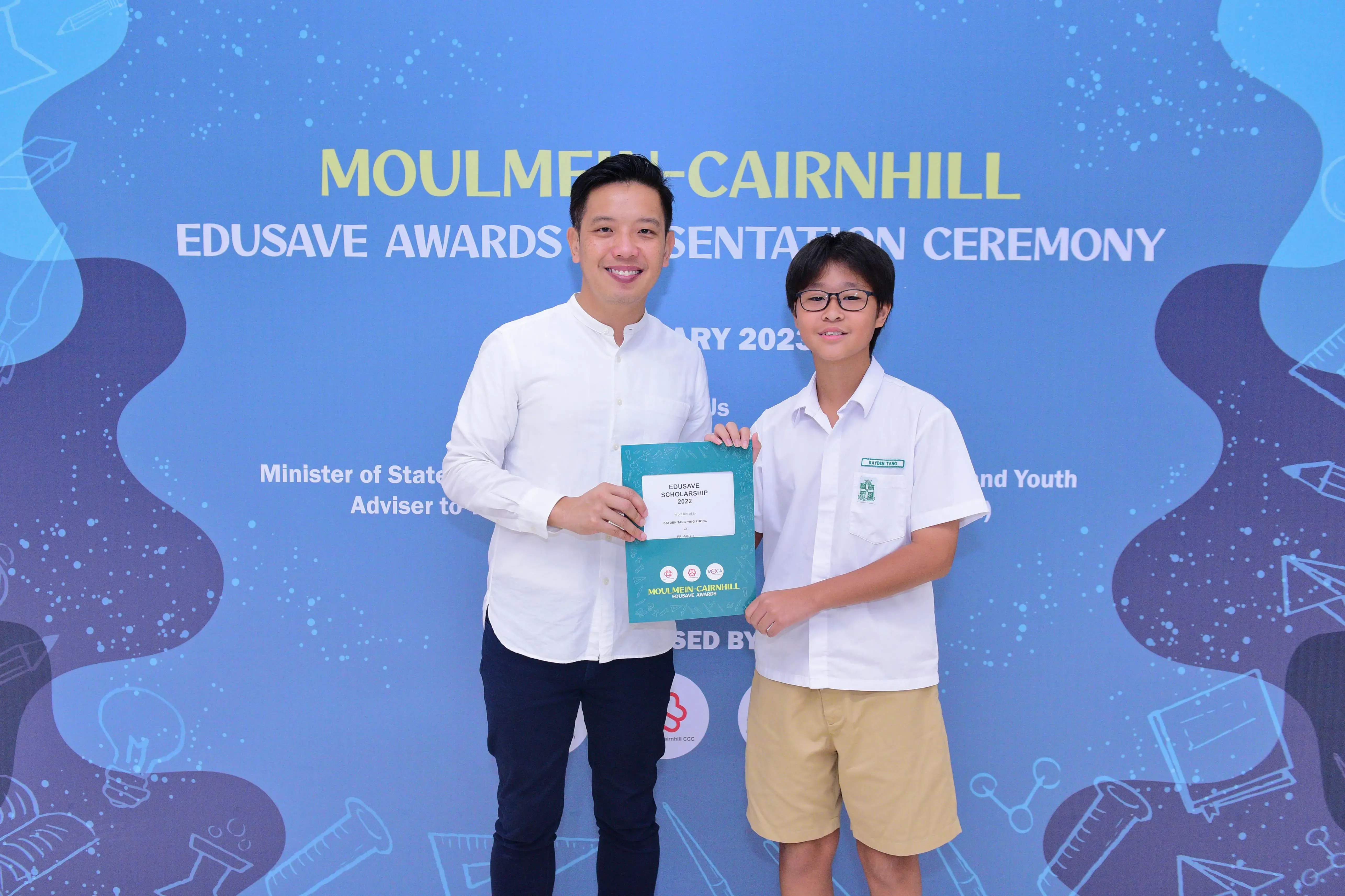 A man and a young student hold an Edusave Scholarship certificate at the Moulmein-Cairnhill Awards Ceremony.