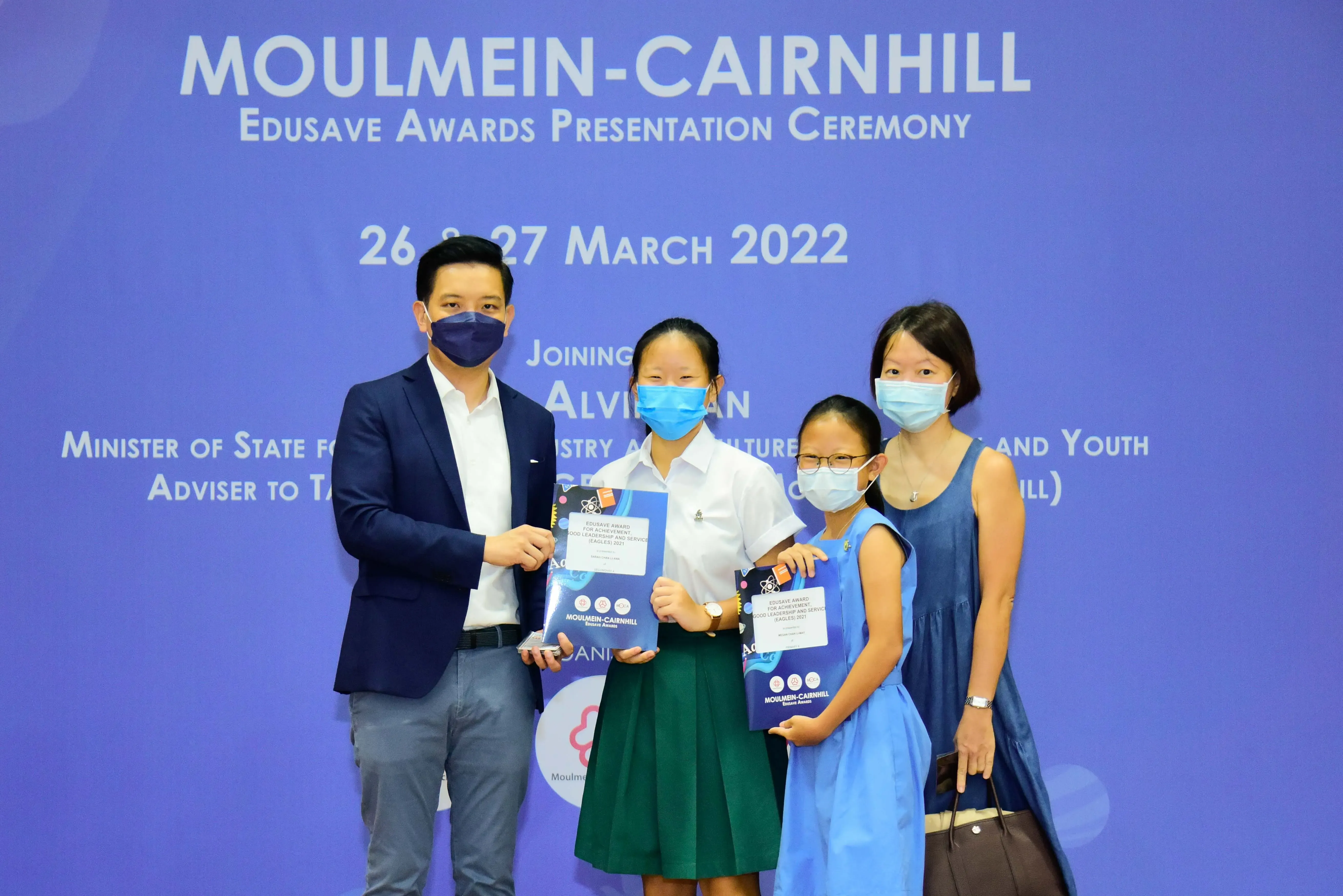 Four masked people pose with award certificates at the Moulmein-Cairnhill Edusave Awards Ceremony, March 2022.