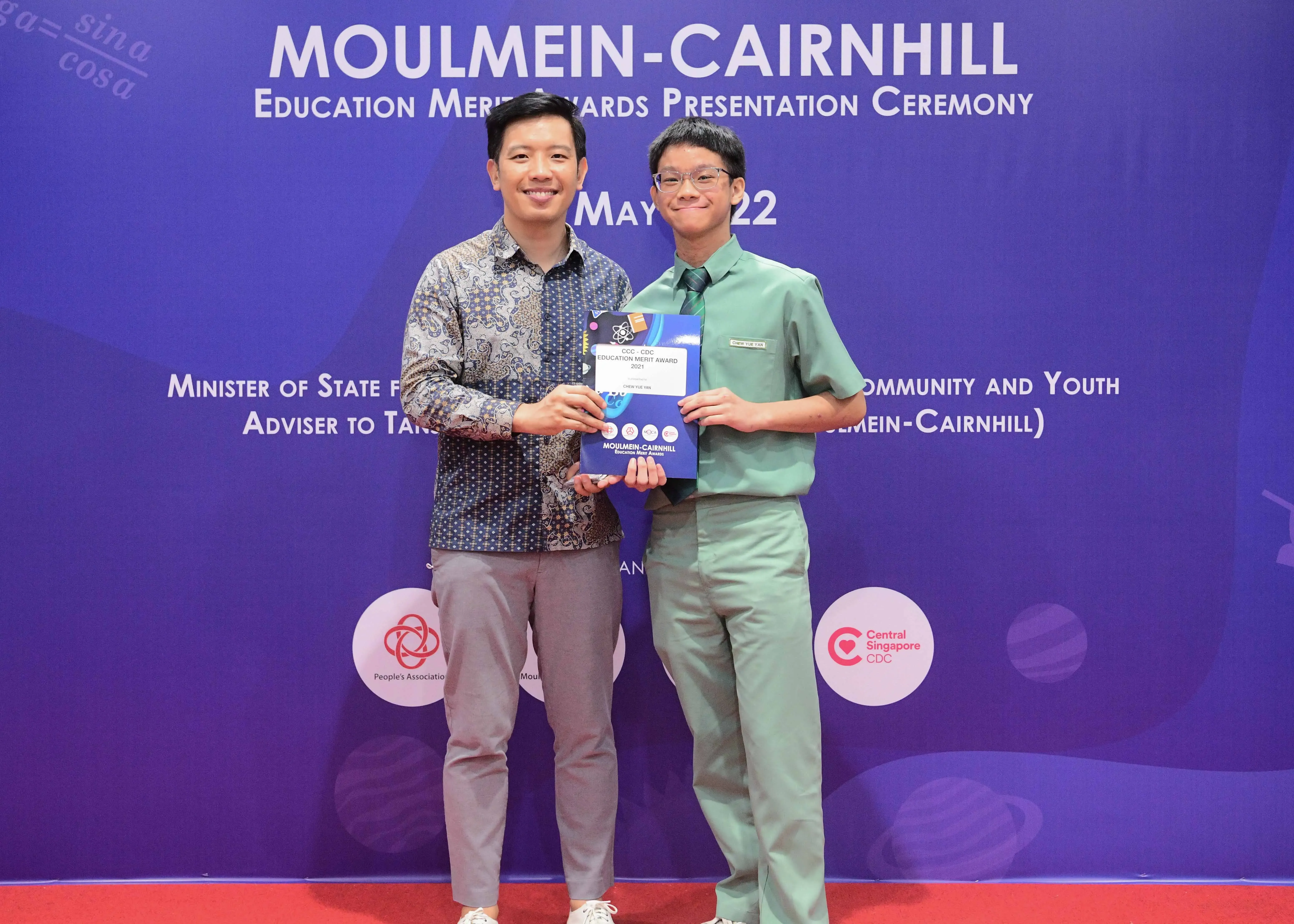 Two men smile holding an award certificate at the Moulmein-Cairnhill Education Merit Awards Presentation Ceremony.