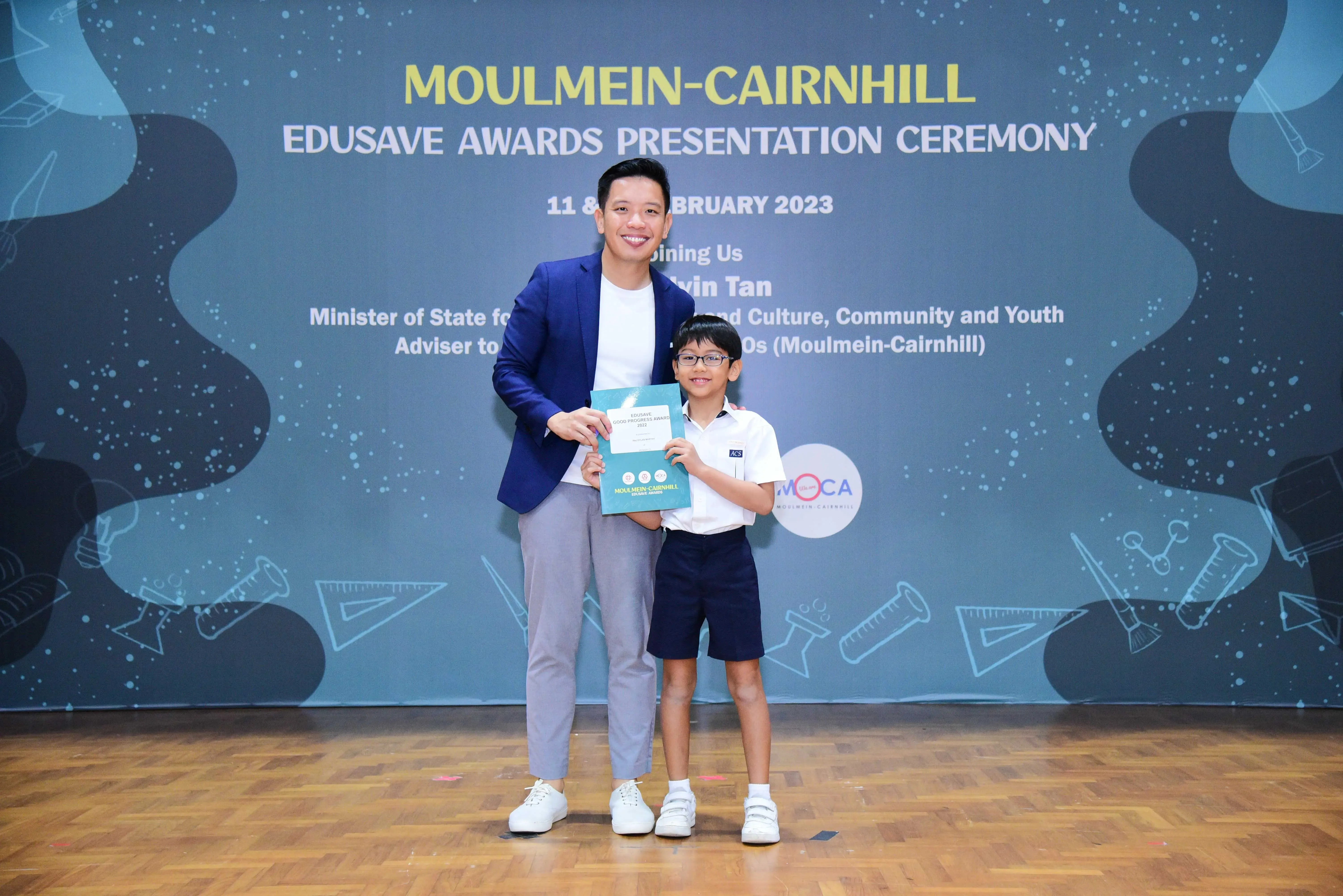 Man in blue blazer and young boy in school uniform holding a certificate at Moulmein-Cairnhill Edusave Awards 2023.
