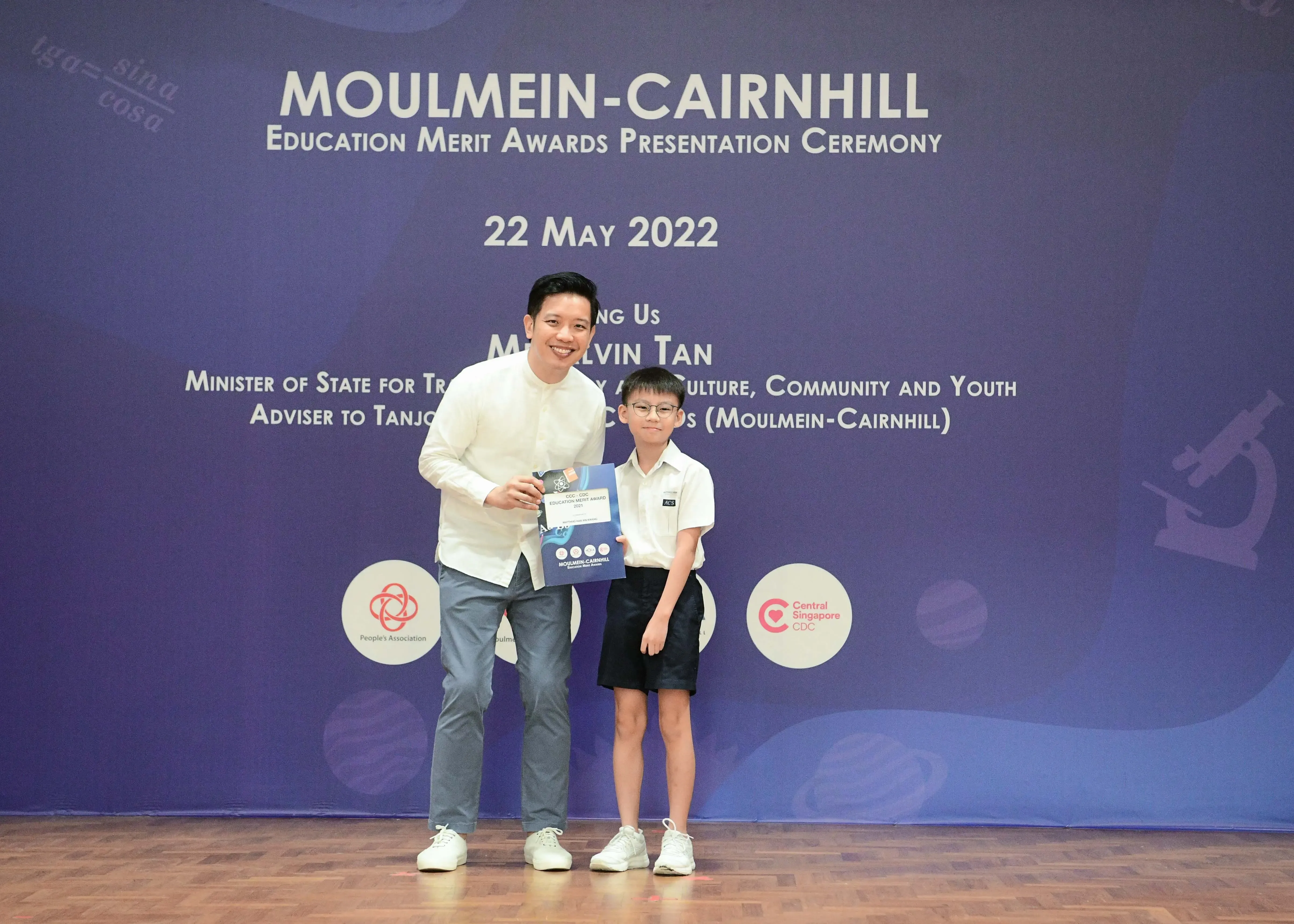 A man and a young boy pose together holding an award booklet at the Moulmein-Cairnhill Education Merit Awards ceremony on 22 May 2022.