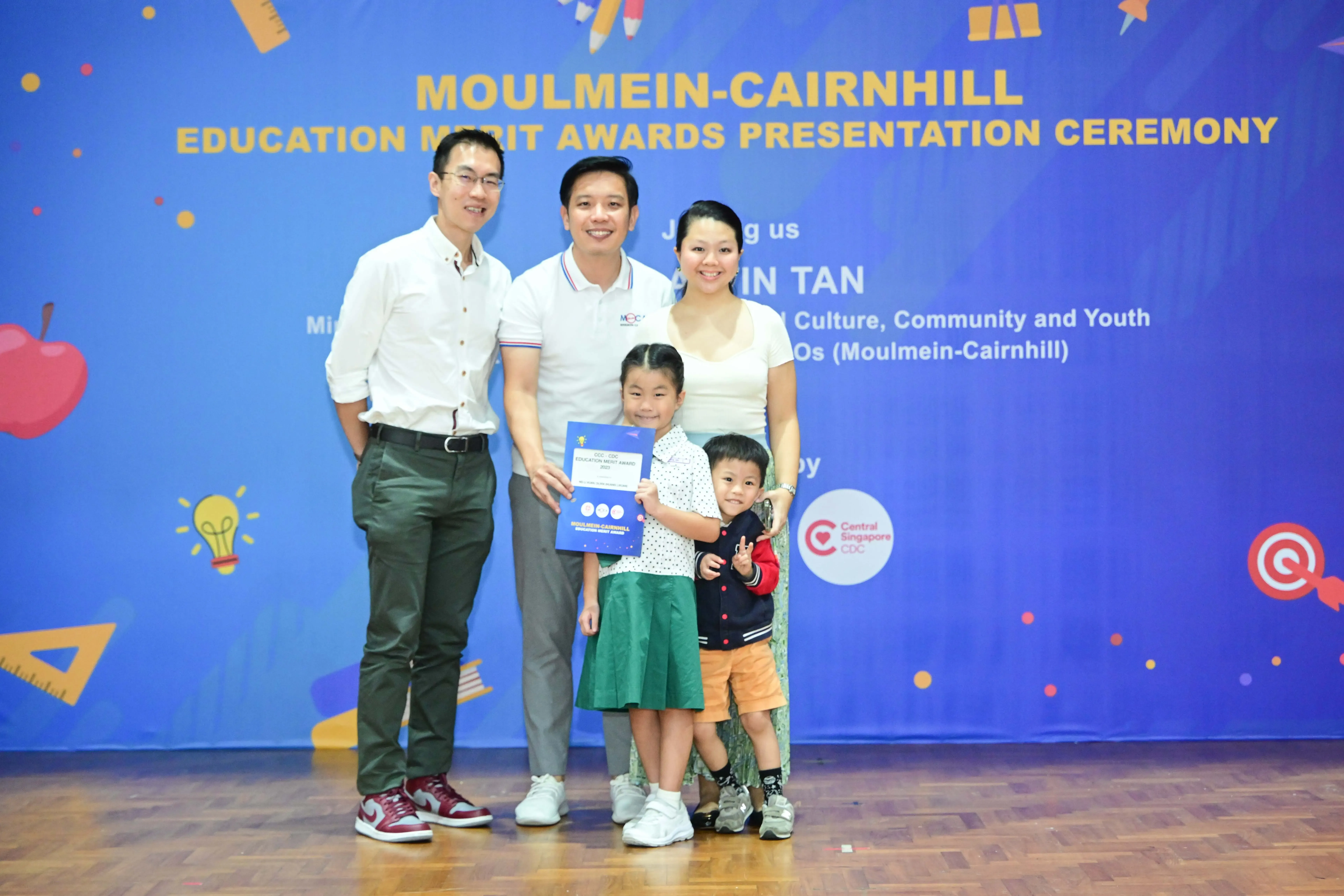 Two adults and two children pose with an award certificate at the Moulmein-Cairnhill Education Merit Awards ceremony.