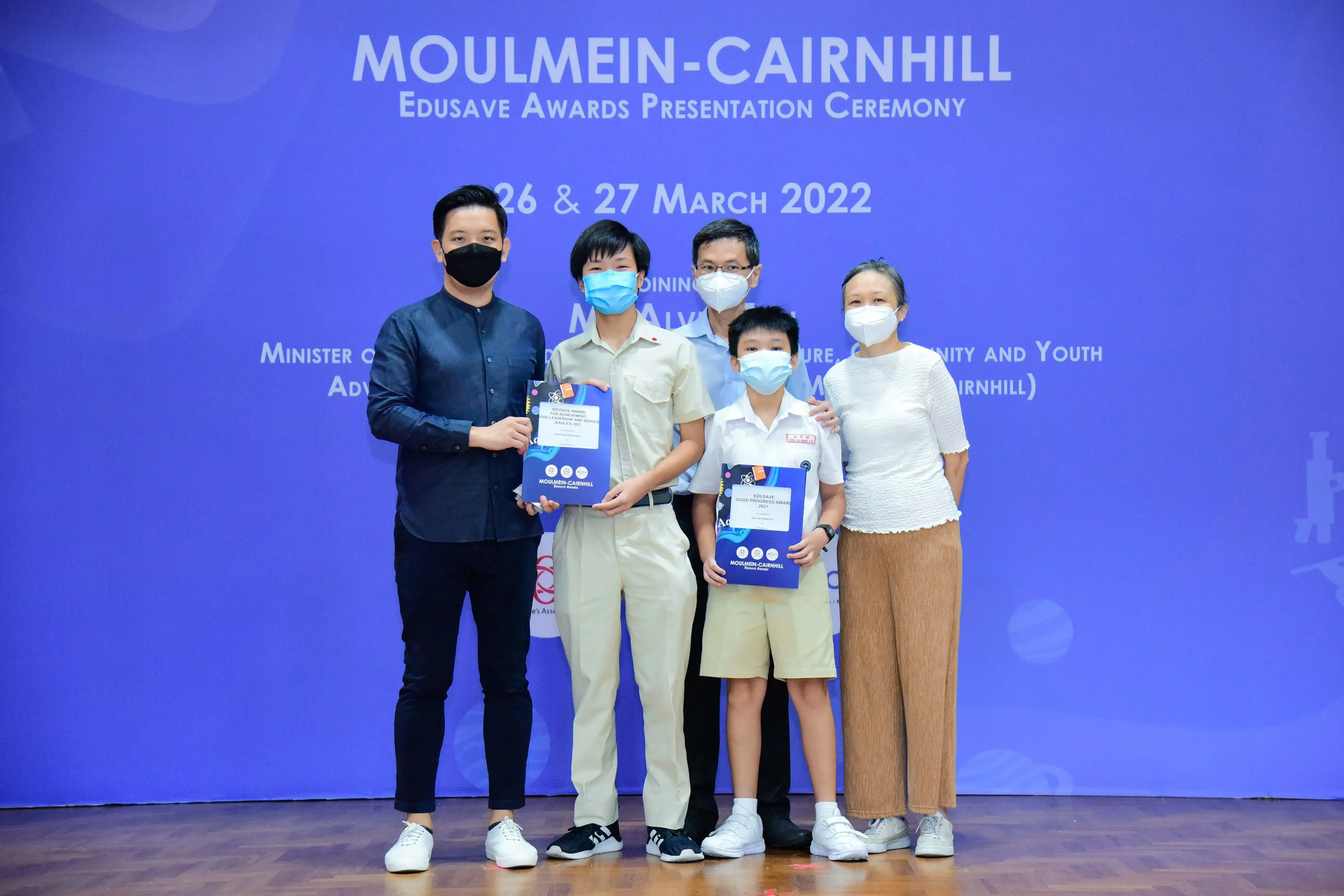 Five masked people pose with award folders at the Moulmein-Cairnhill Edusave Awards Ceremony, March 2022.