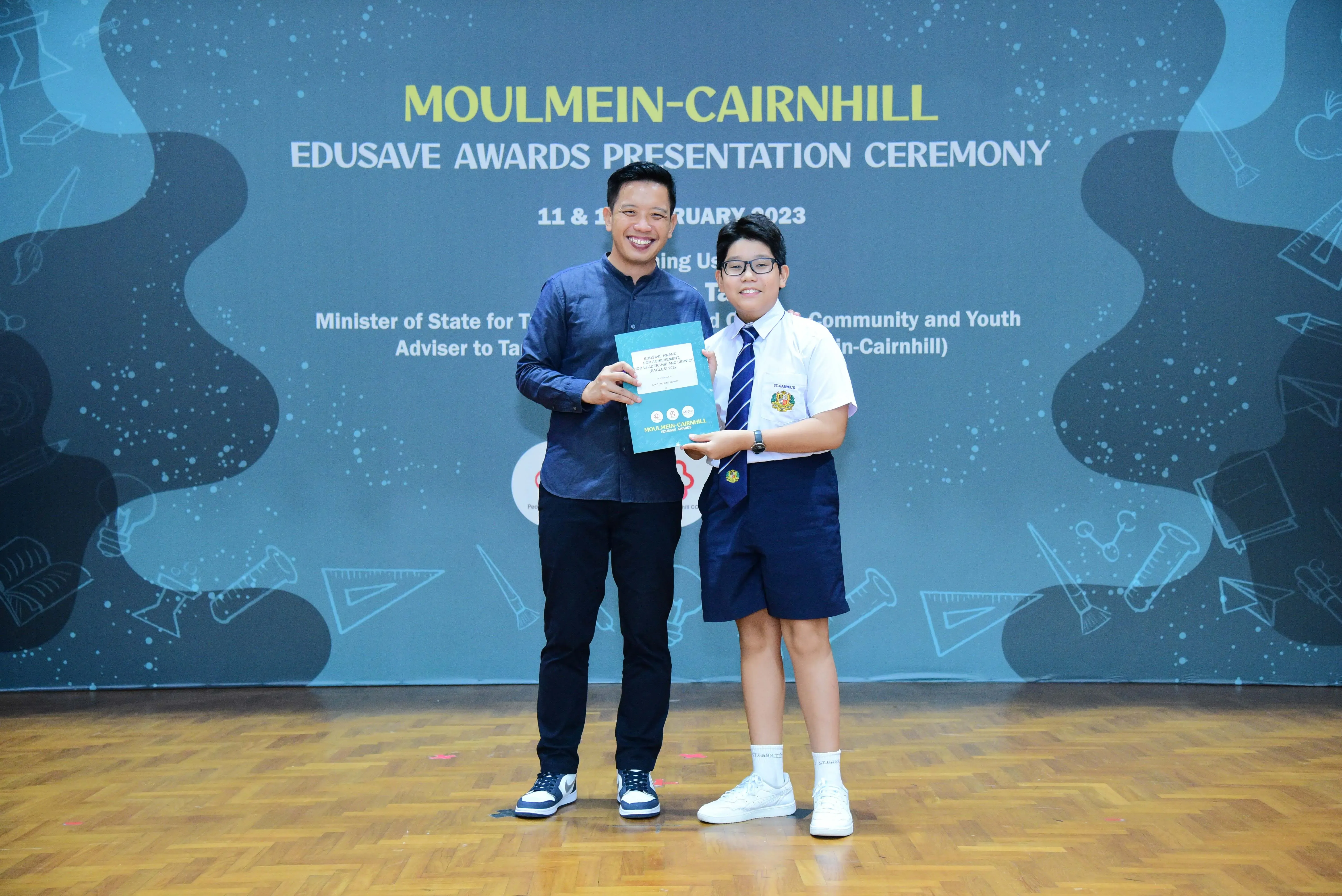 An adult and a uniformed student hold a certificate at the Moulmein-Cairnhill Edusave Awards Ceremony 2023.