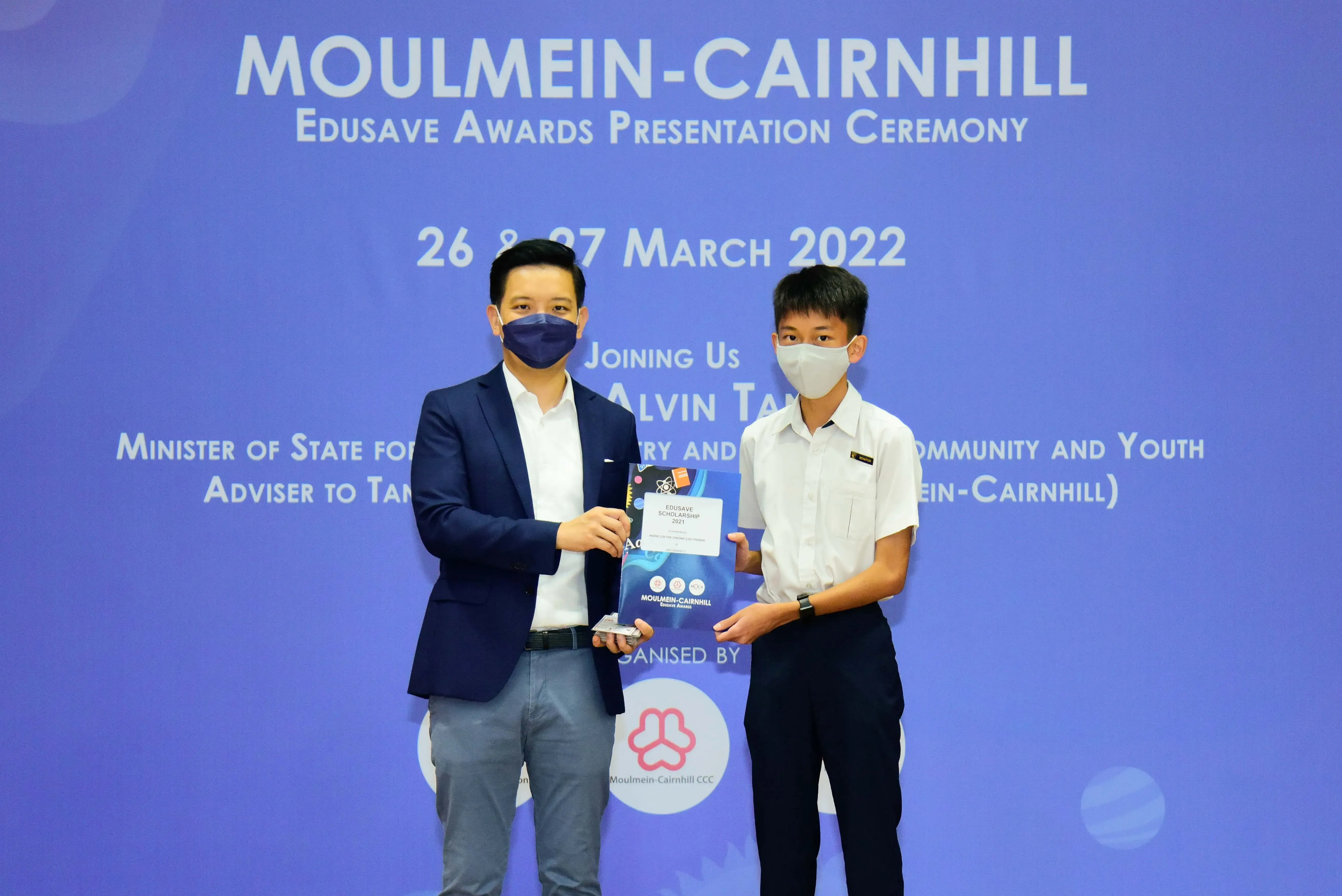 Two masked men hold an award together at the Moulmein-Cairnhill Edusave Awards Ceremony, March 2022.