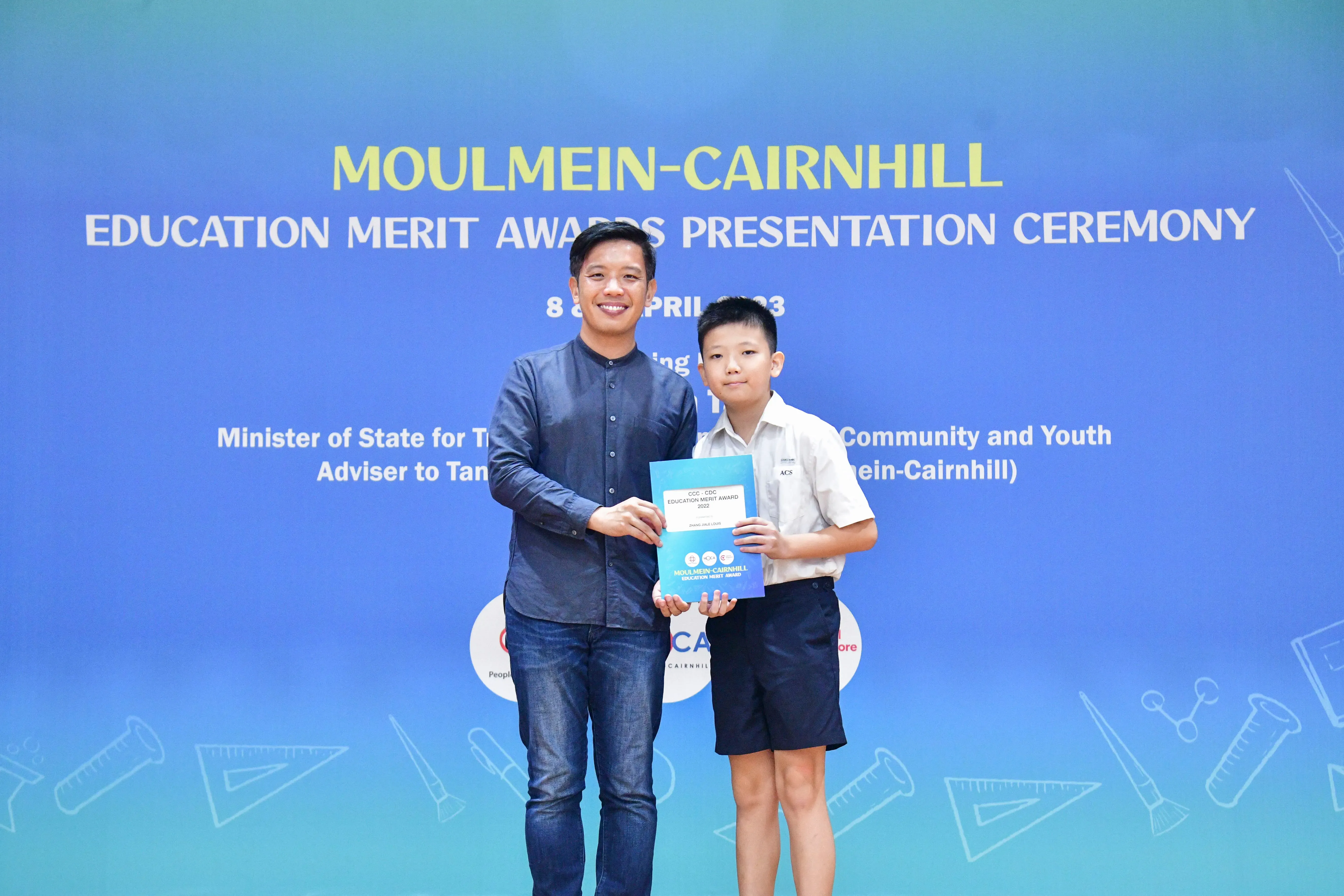 An adult and a young boy hold a certificate together at the Moulmein-Cairnhill Education Merit Awards Ceremony.