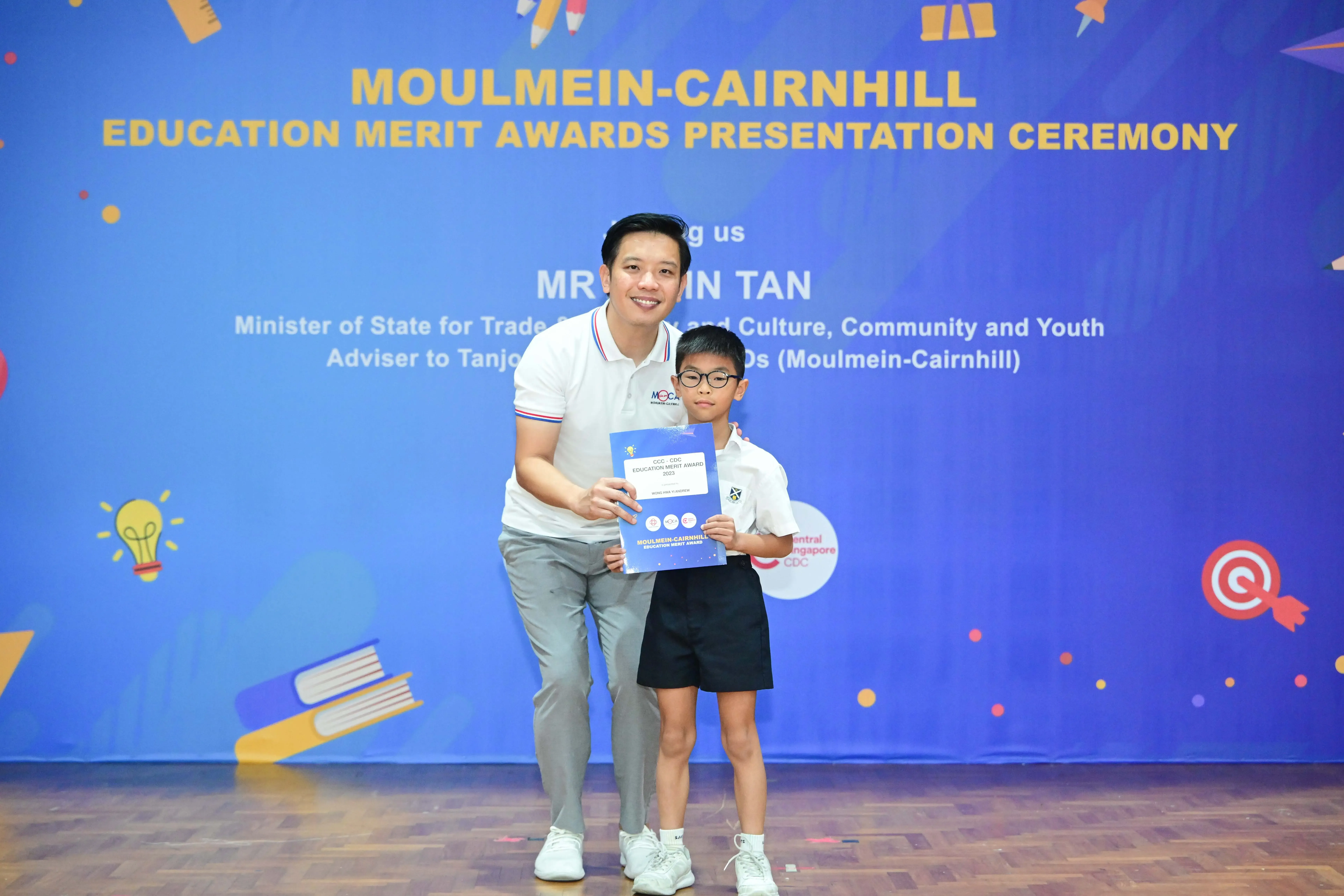 A man and a young student hold a certificate together at the Moulmein-Cairnhill Education Merit Awards ceremony.