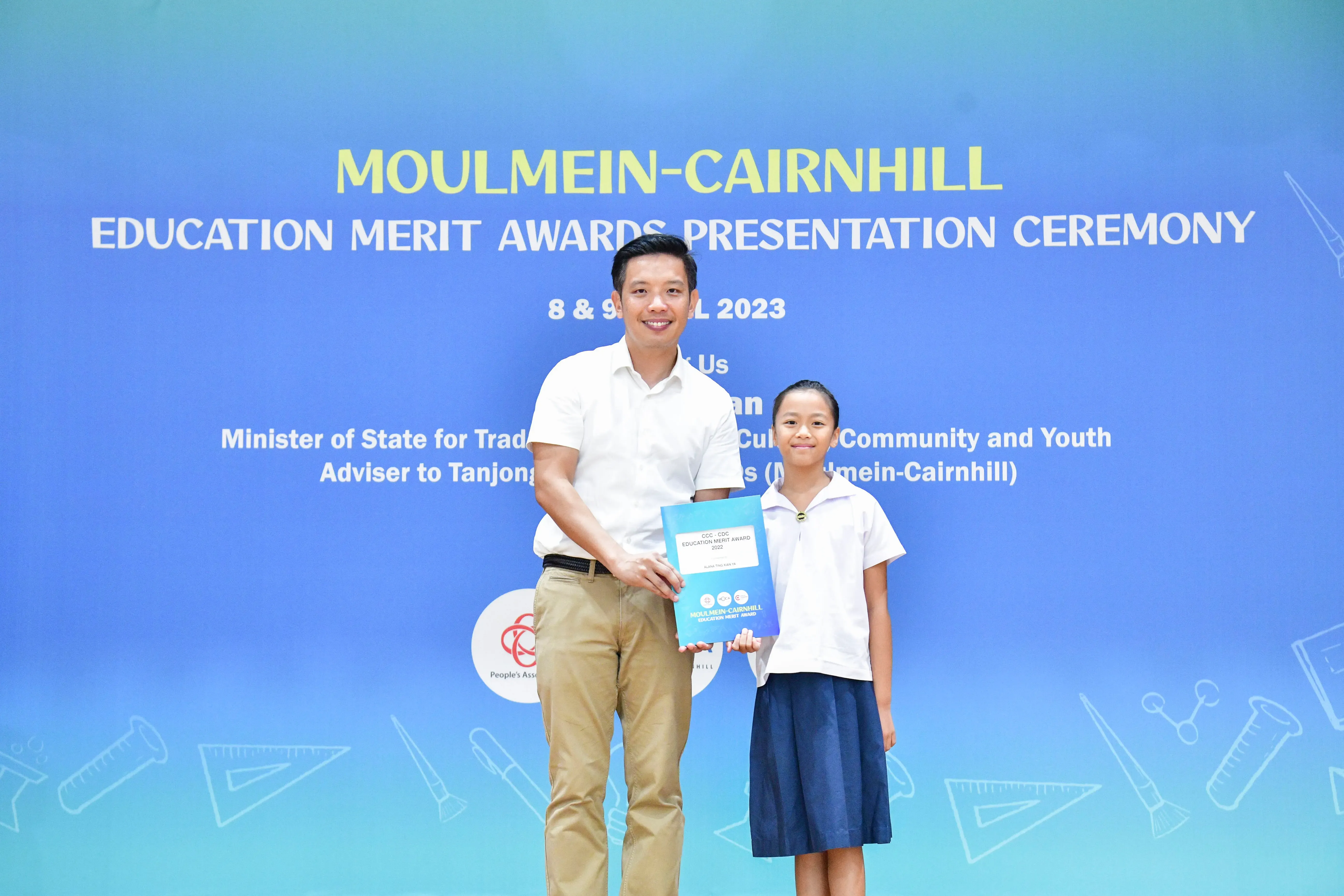 A man and a young girl hold an award certificate at the Moulmein-Cairnhill Education Merit Awards Ceremony 2023.