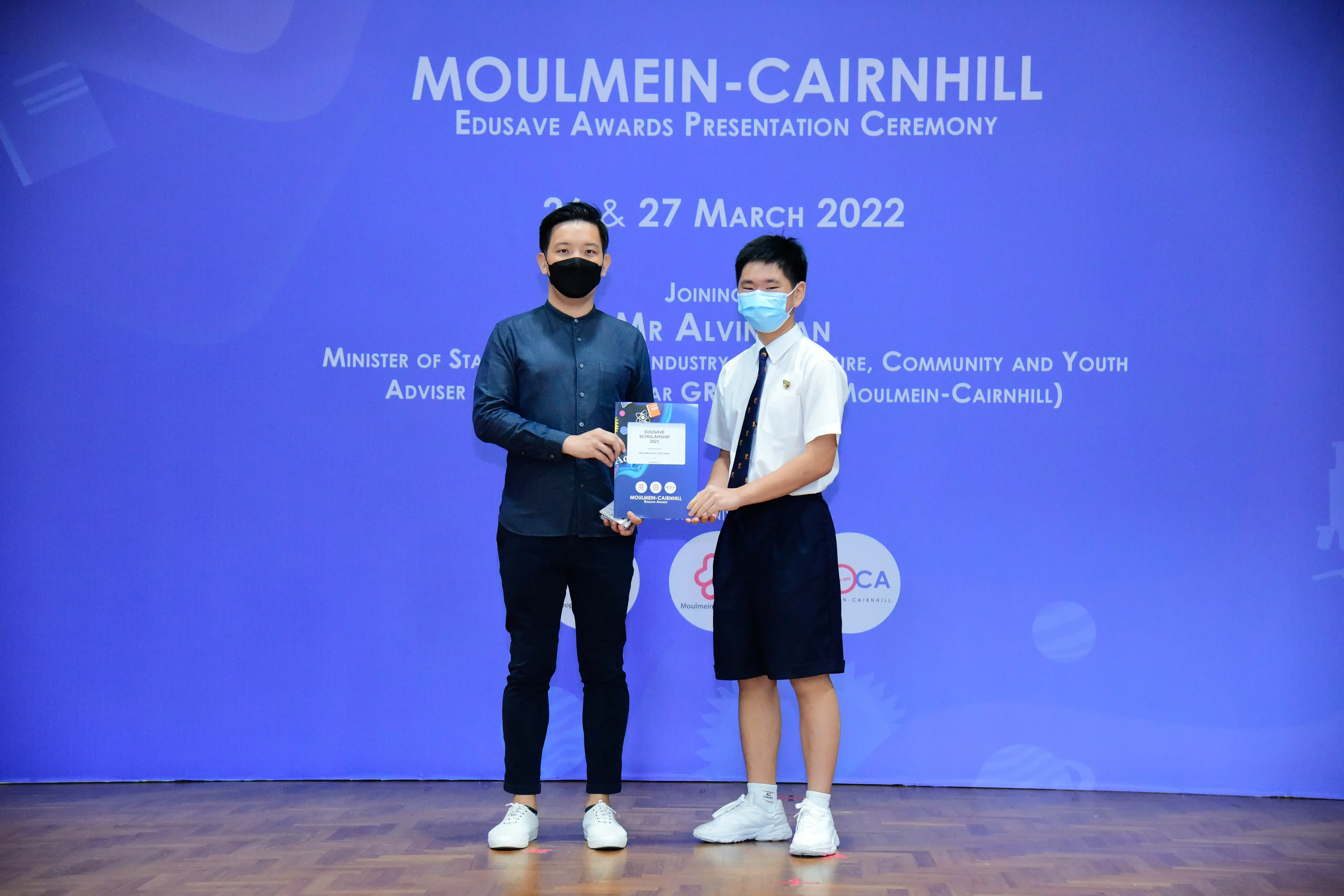 Two masked individuals hold an award booklet at the Moulmein-Cairnhill Edusave Awards Ceremony, March 2022.
