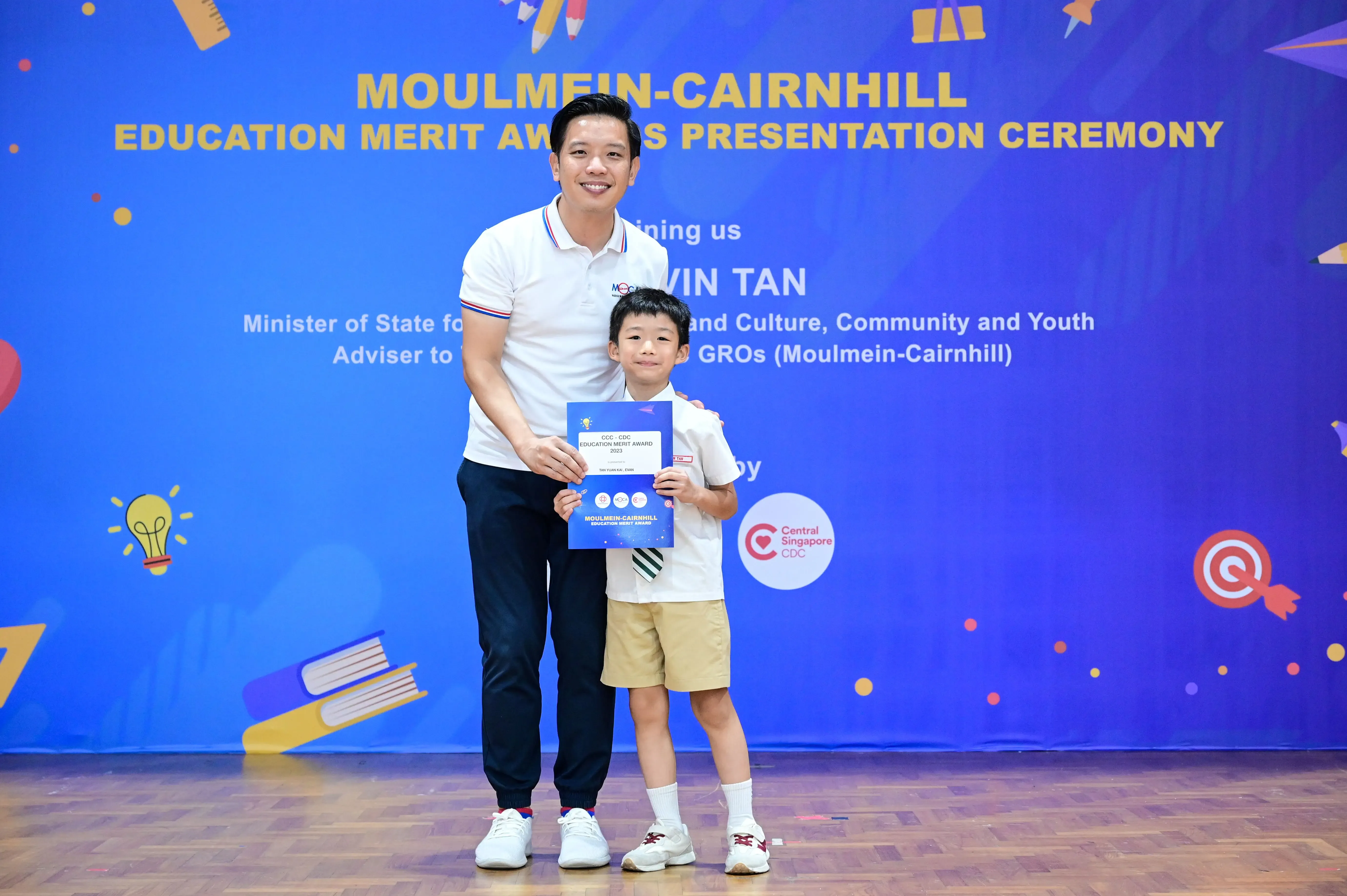 A man and a young boy pose holding a certificate at the Moulmein-Cairnhill Education Merit Awards ceremony.