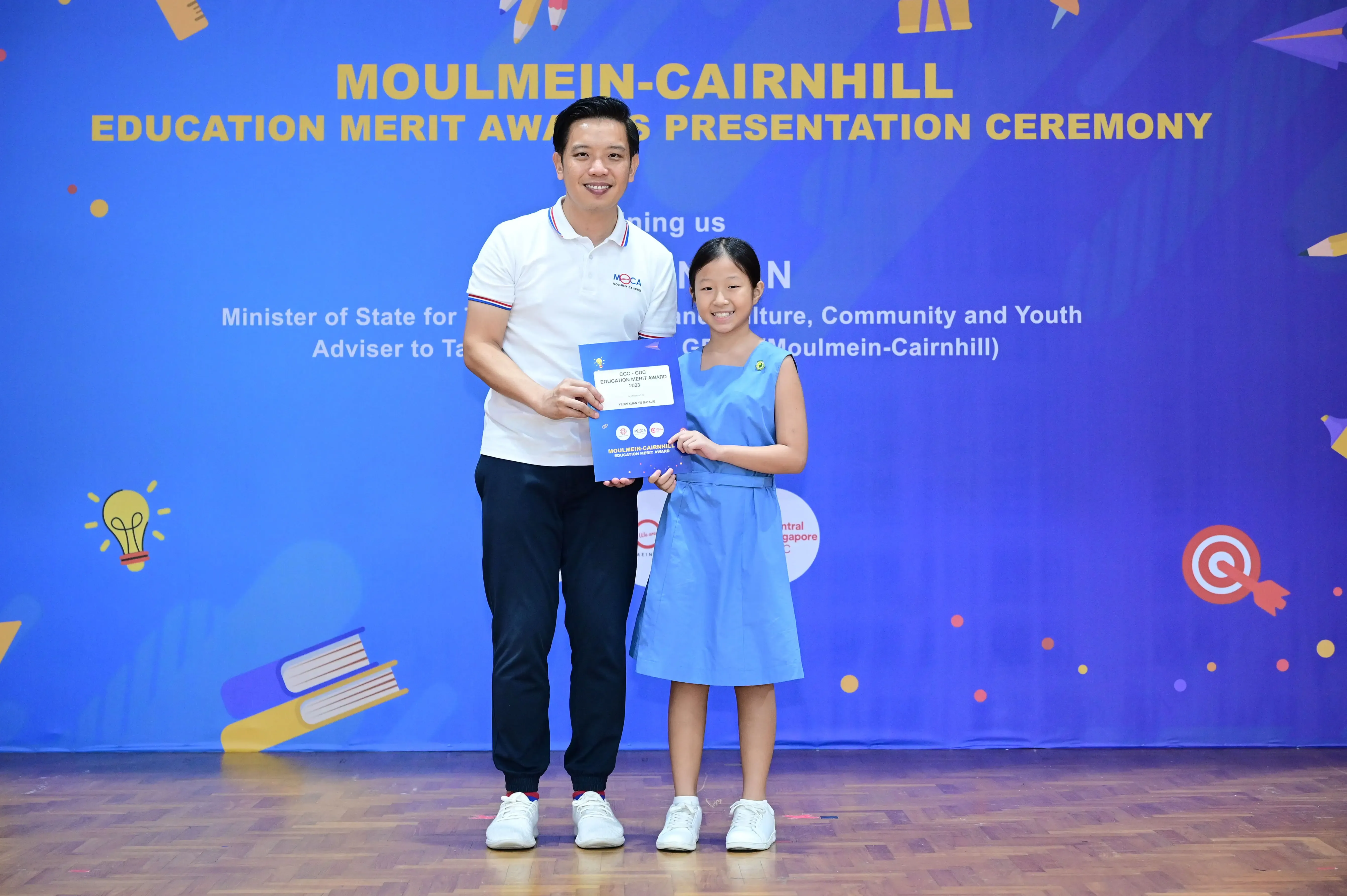 A man and a young girl hold an award certificate at the Moulmein-Cairnhill Education Merit Awards Presentation Ceremony.