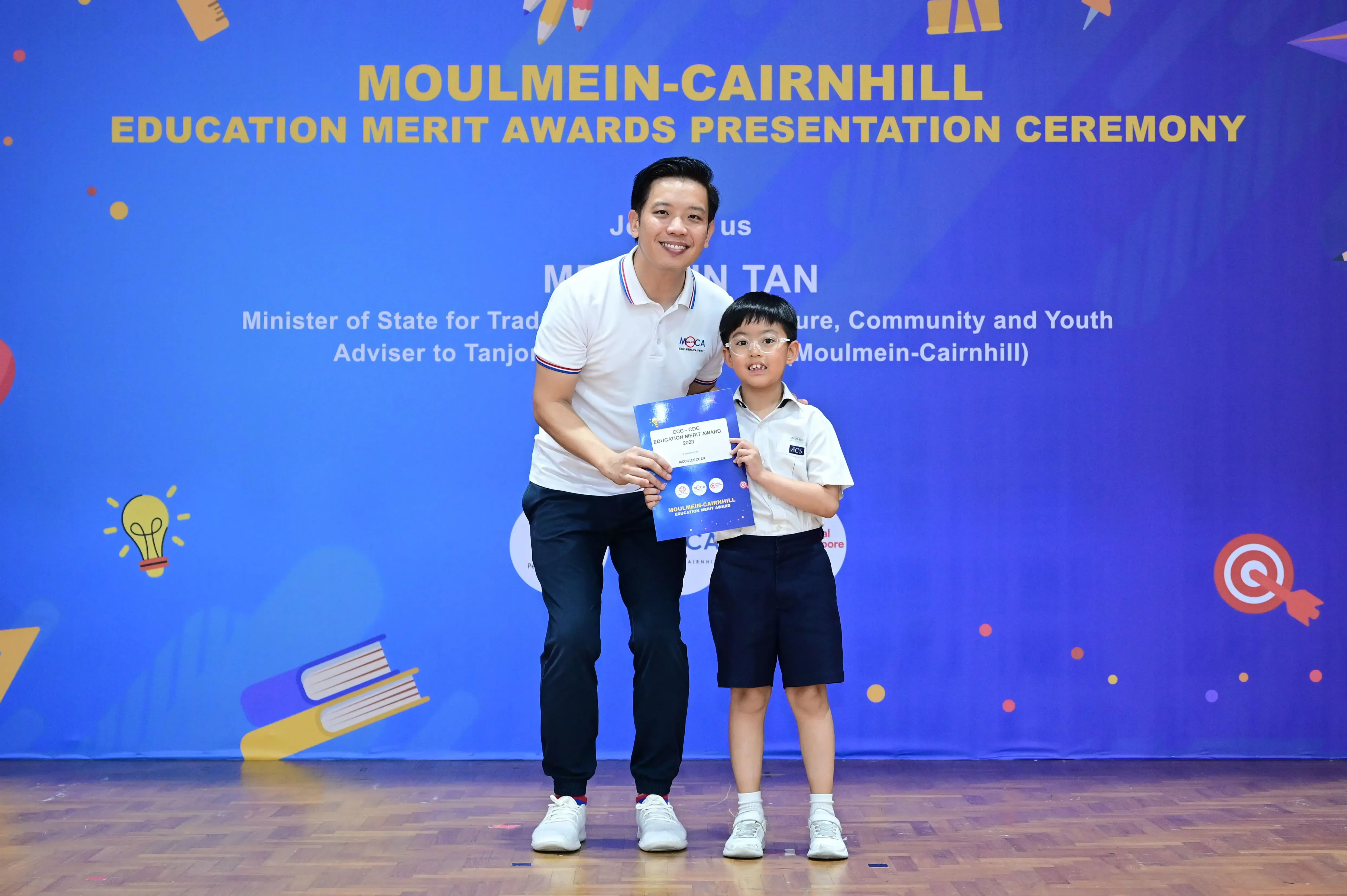 Adult man and young boy holding a certificate at Moulmein-Cairnhill Education Merit Awards Presentation Ceremony.