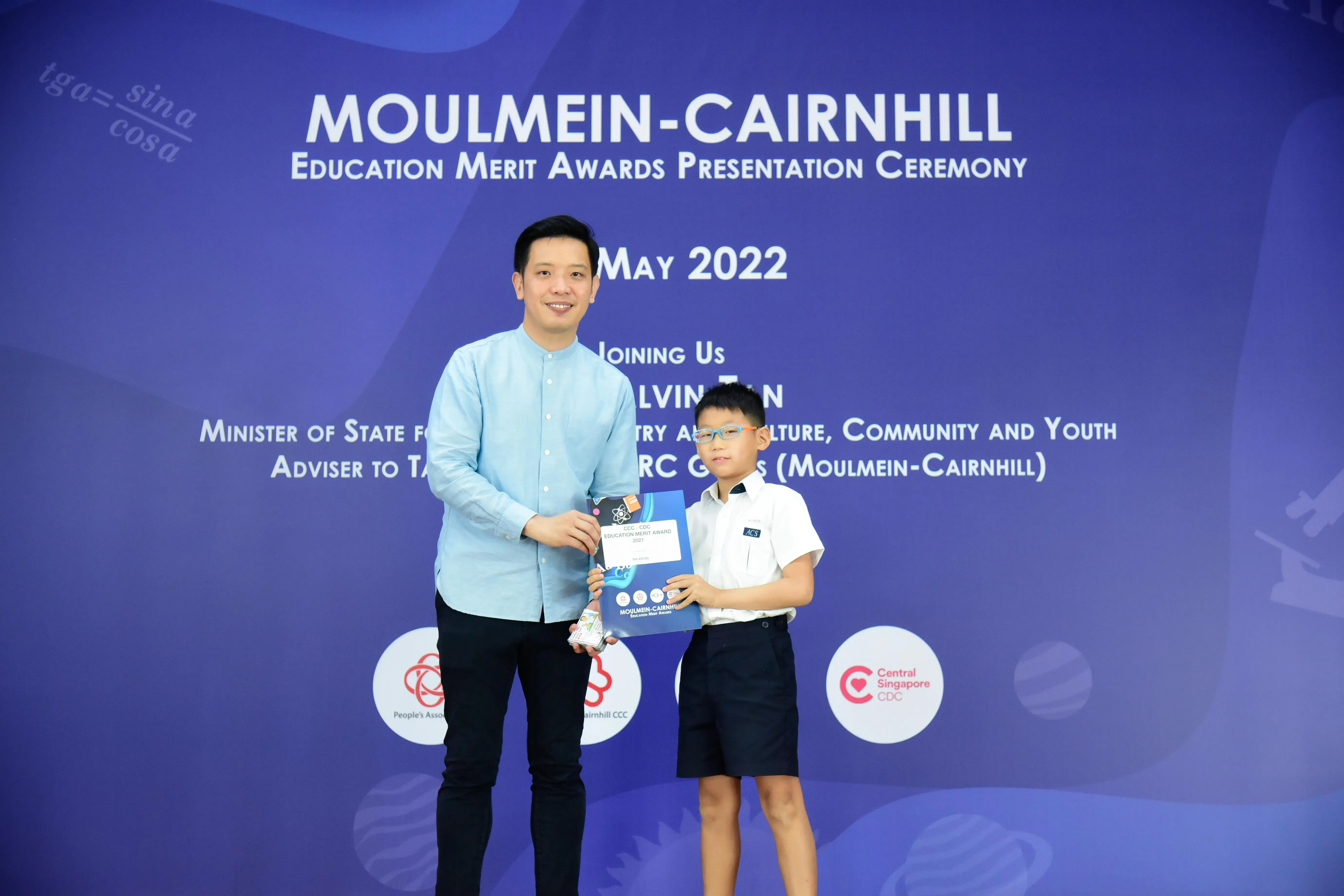 A man and a young boy hold an award certificate at the Moulmein-Cairnhill Education Merit Awards Ceremony, May 2022.