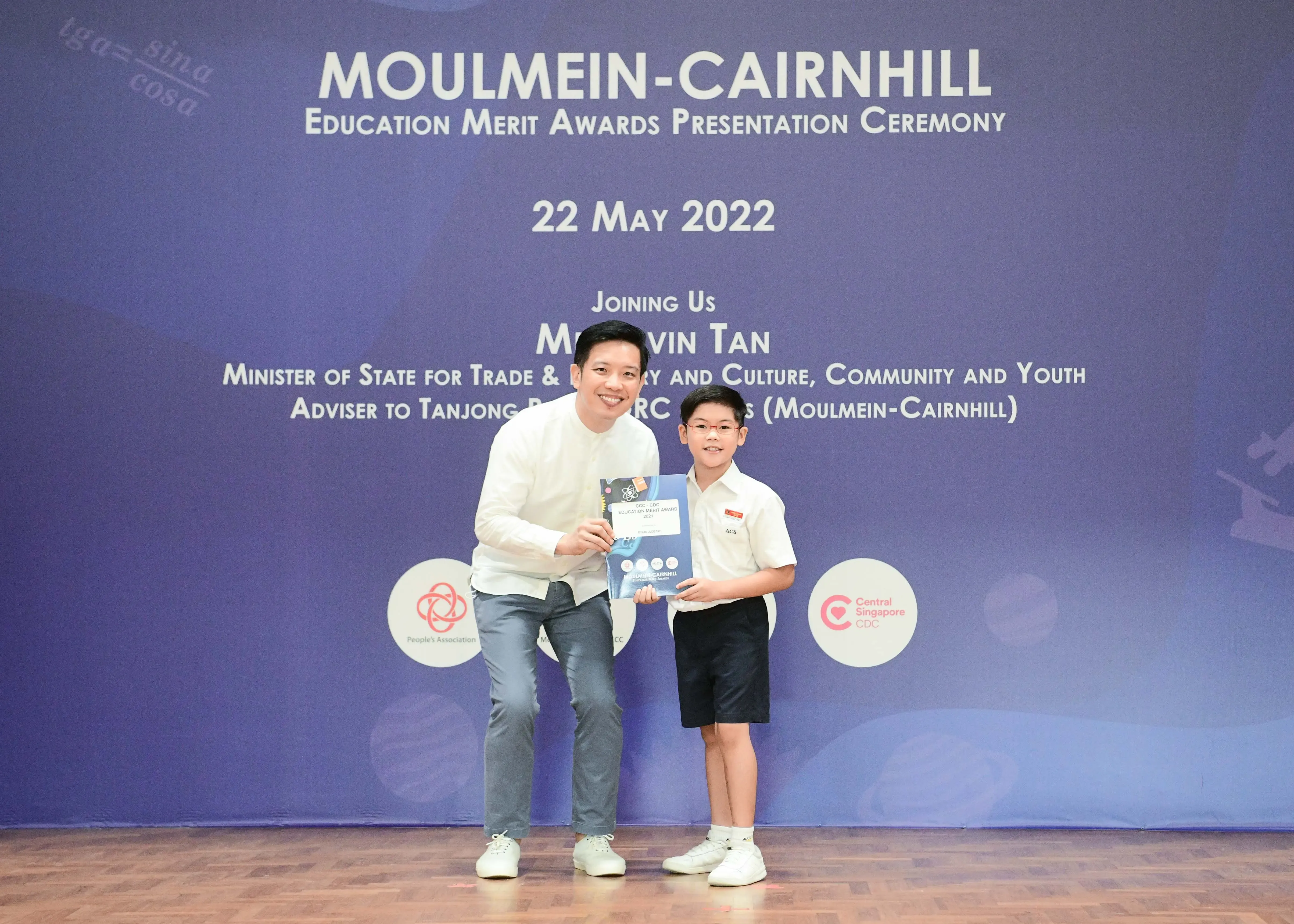 An adult and a young boy hold an award certificate at the Moulmein-Cairnhill Education Merit Awards ceremony on 22 May 2022.