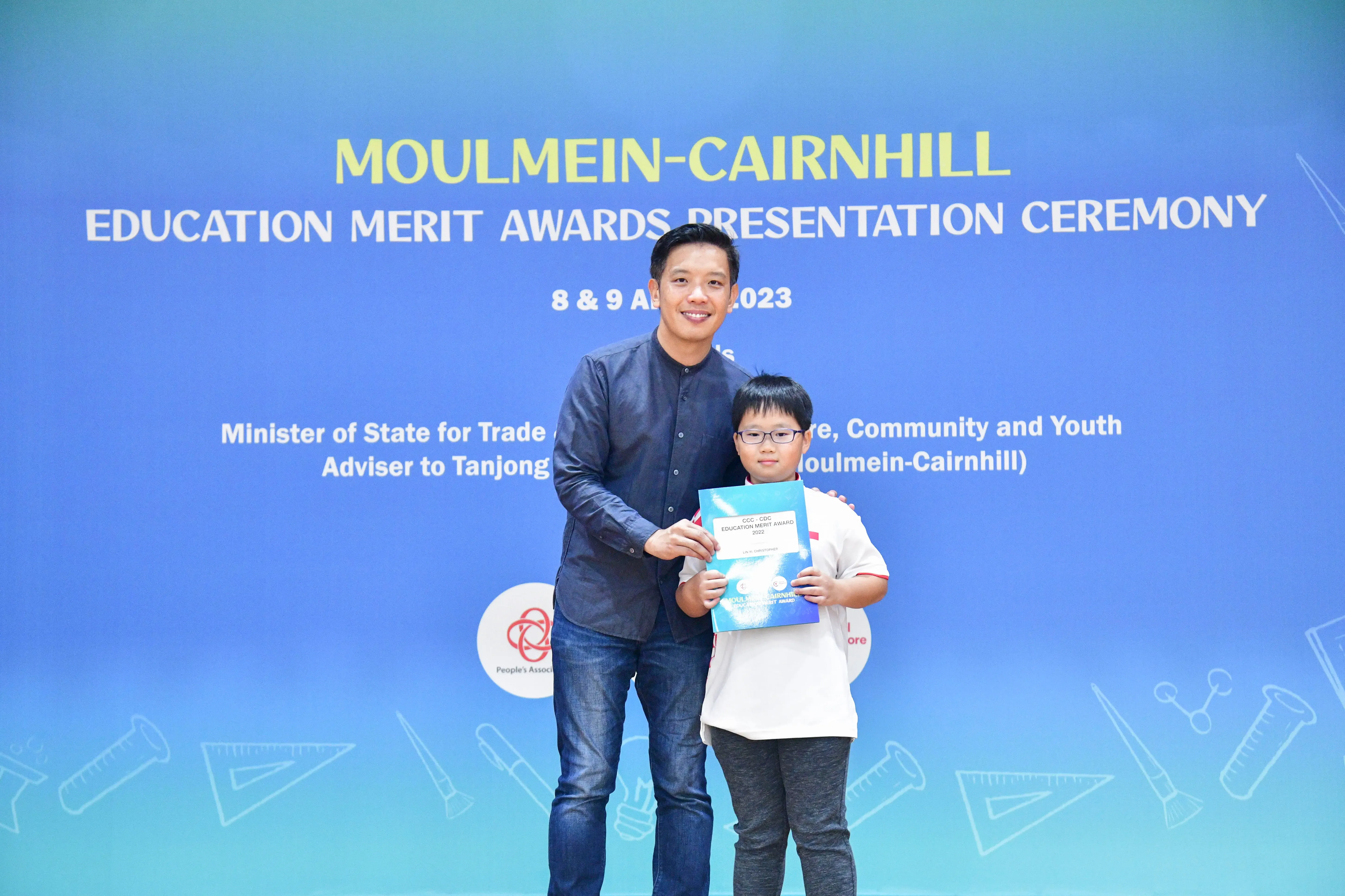 An adult and a young boy holding an award booklet at the Moulmein-Cairnhill Education Merit Awards Ceremony 2023.